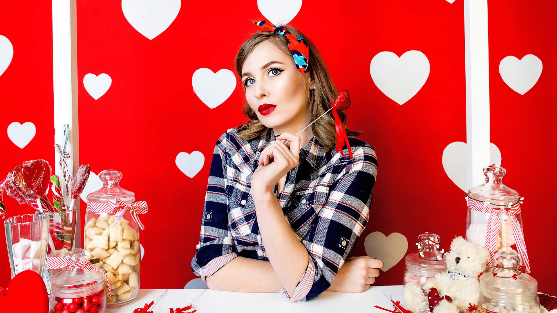 Яркая девушка за столом со сладостями на красном фоне с белыми сердечками 