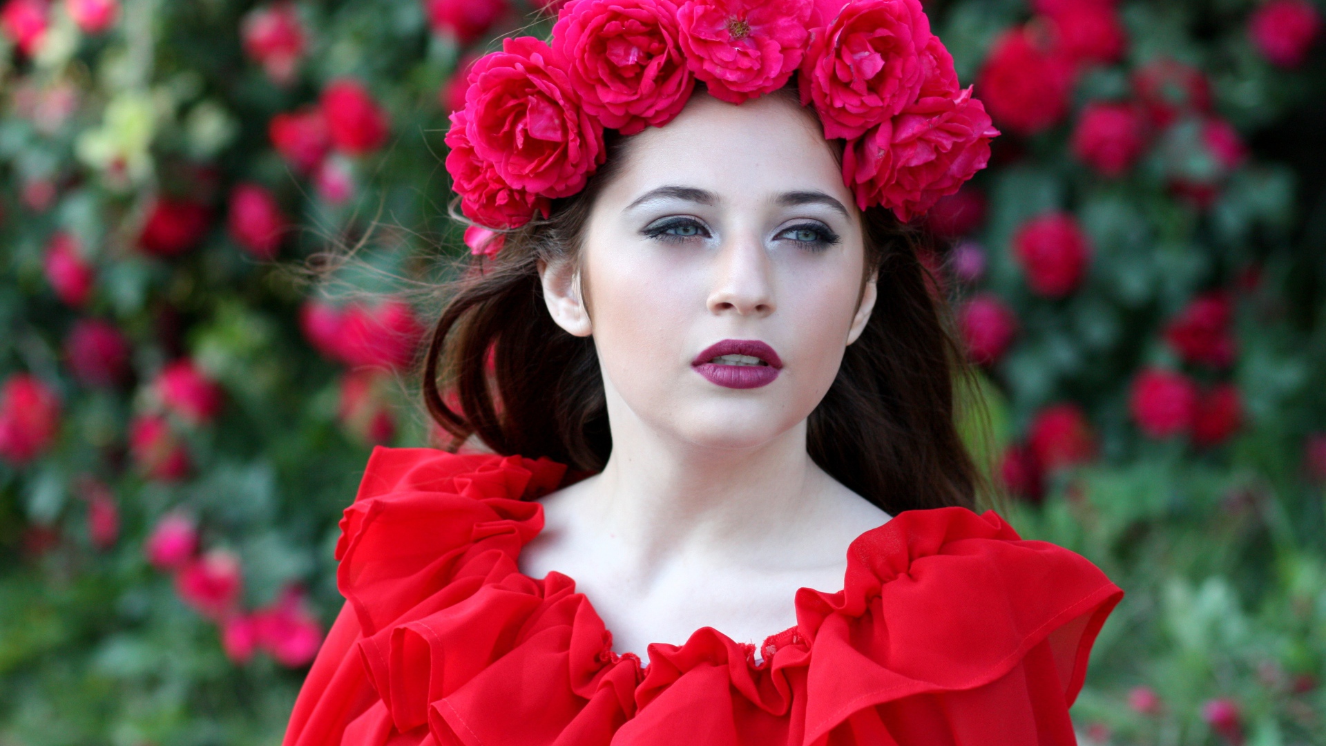 Яркая девушка в красном платье с венком из роз на голове