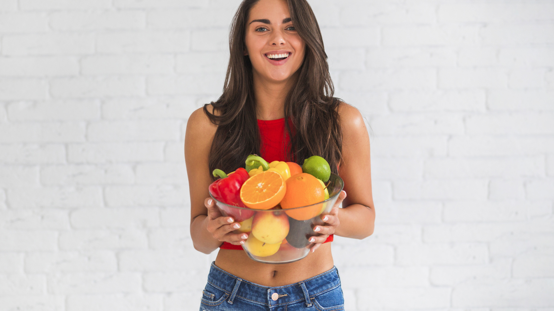 Брюнетка с миской фруктов на фоне стены