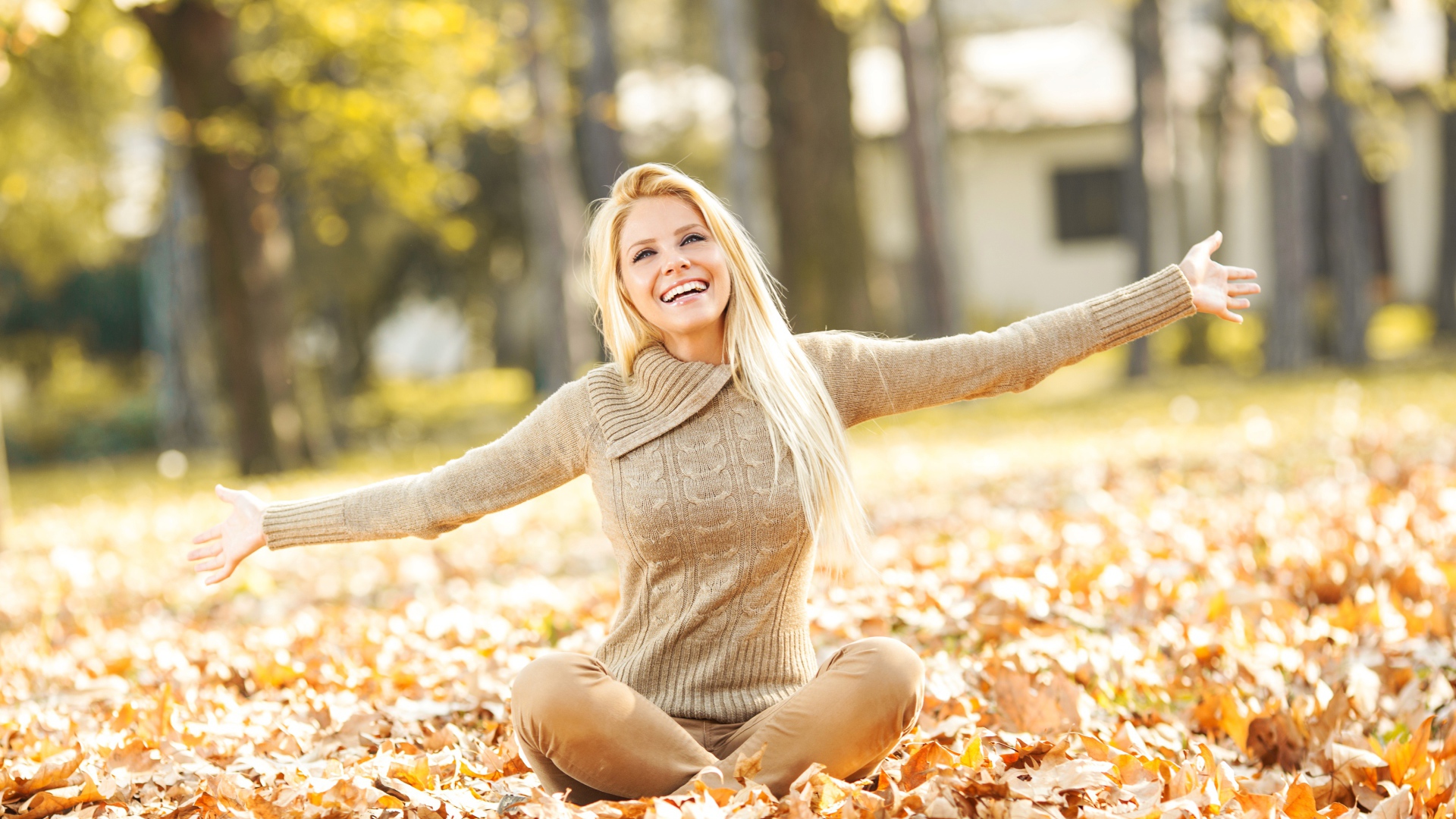 Веселая девушка сидит на опавшей листве осенью 