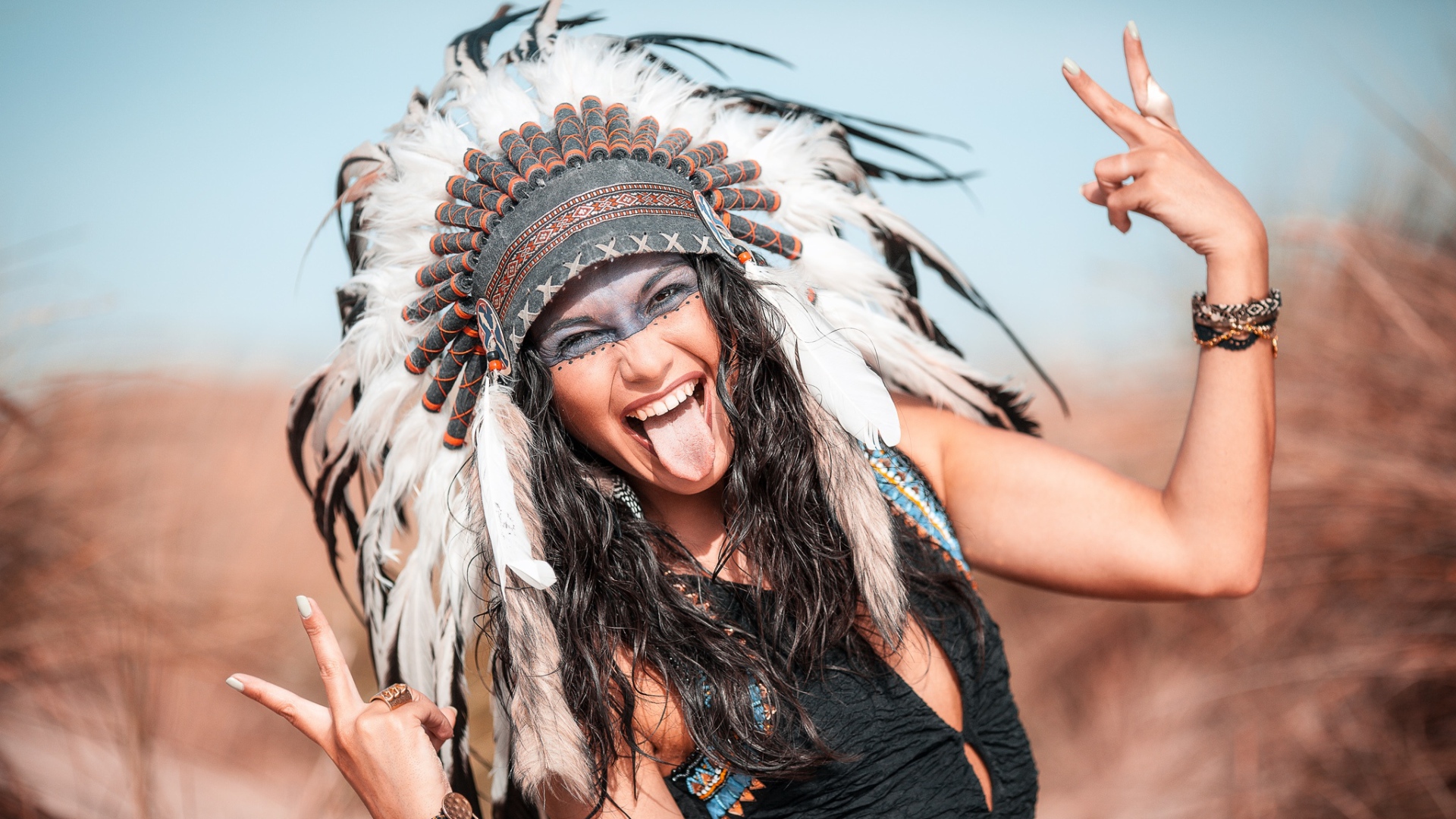 Веселая девушка с высунутым языком в костюме индейца