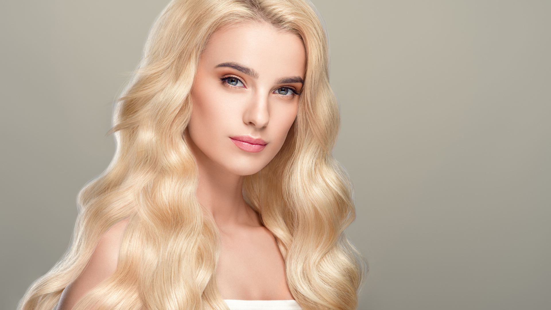 Милая длинноволосая блондинка на сером фоне