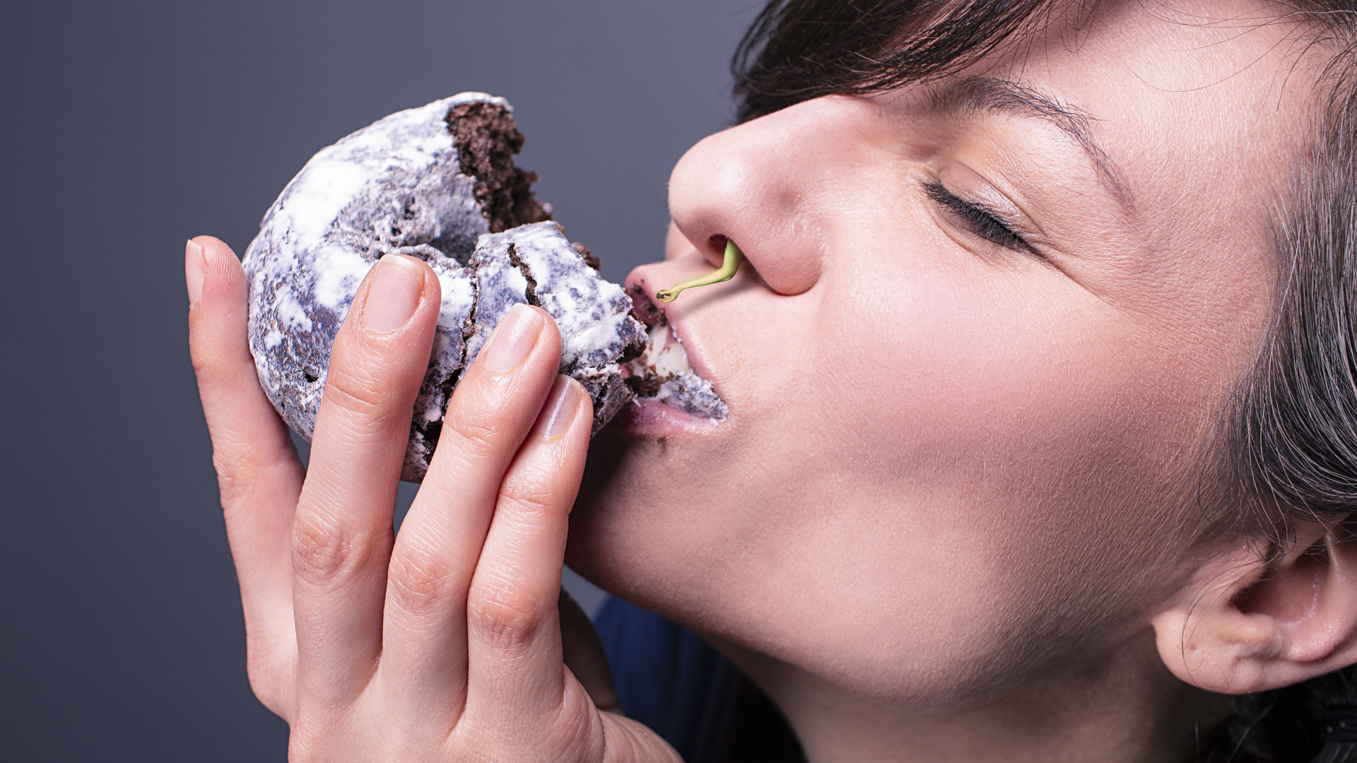 Девушка ест шоколадный пряник на сером фоне