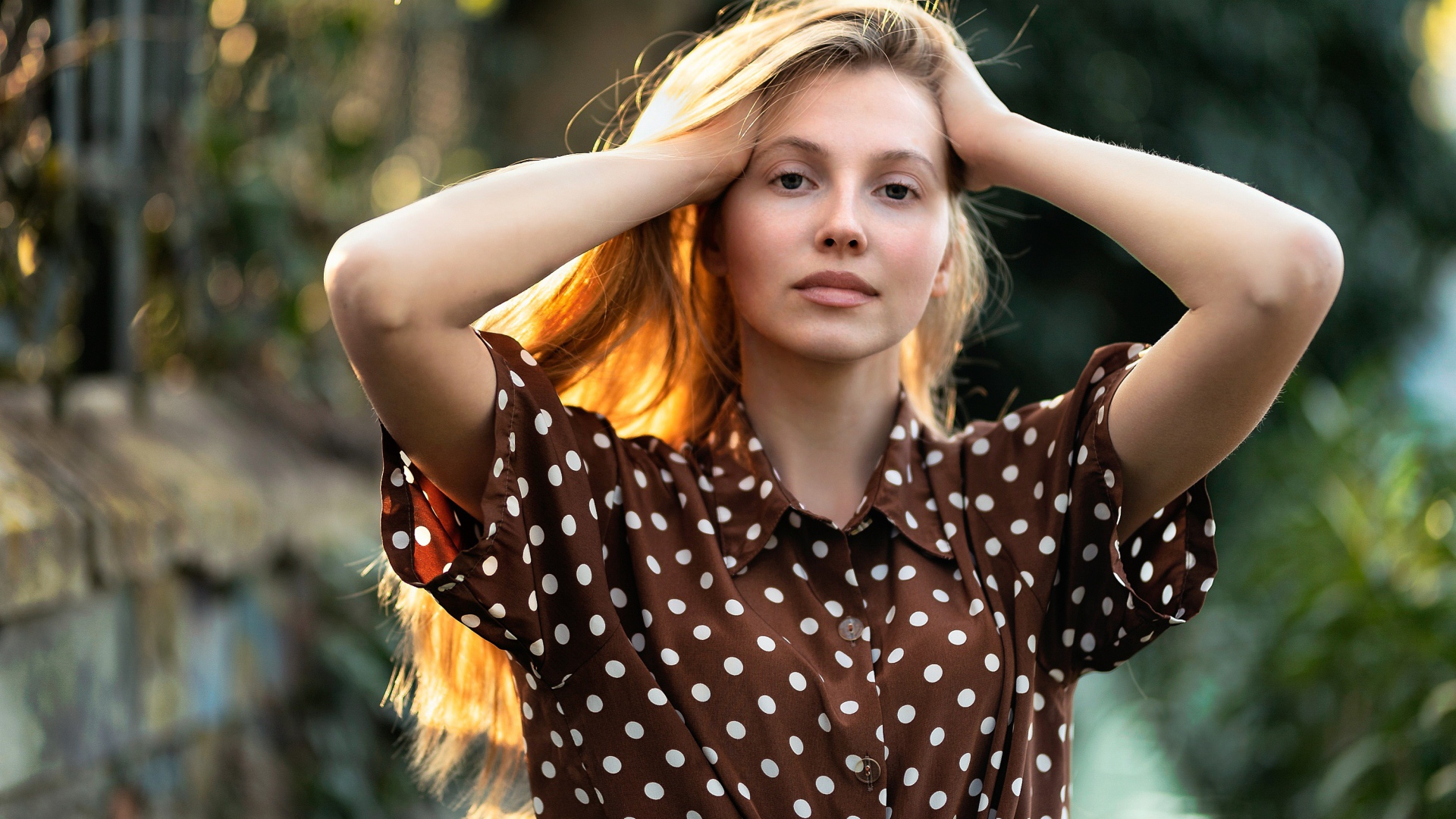 Девушка в рубашке в горох с руками в волосах 