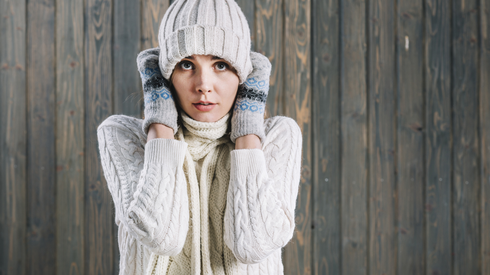 Девушка в варежках поправляет шапку на голове