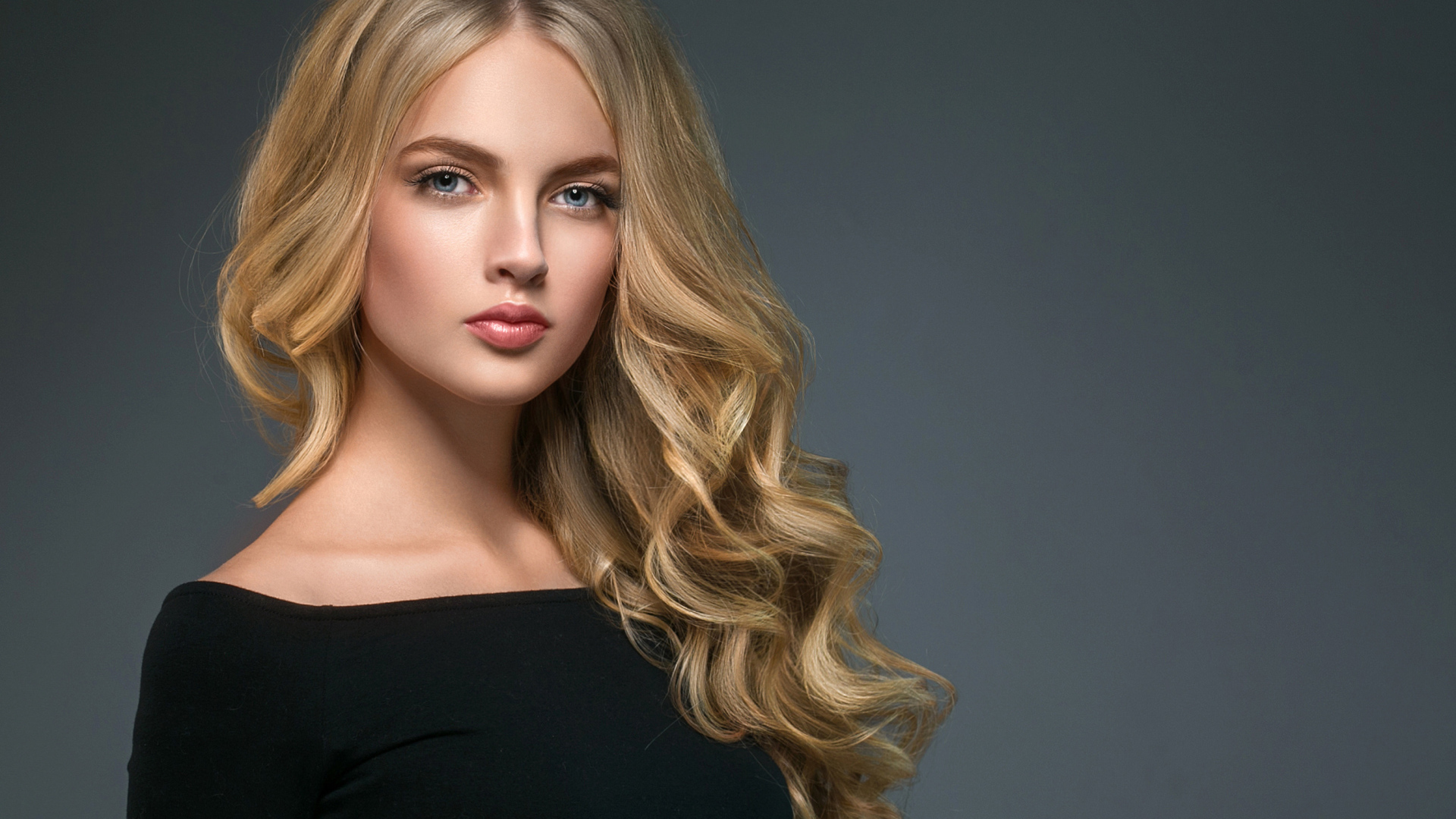 Длинноволосая блондинка с голубыми глазами на сером фоне