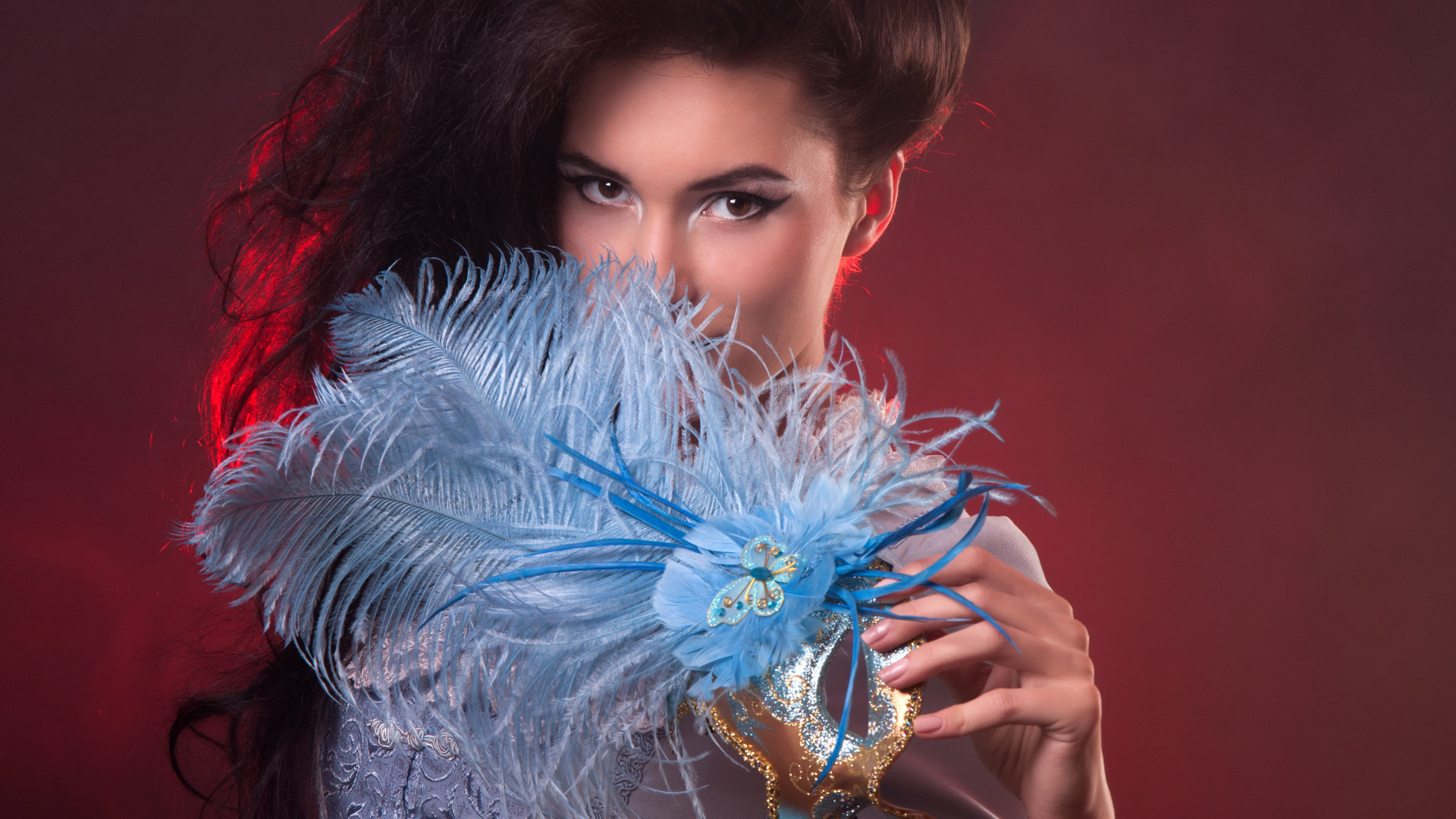 Длинноволосая девушка с маской с перьями в руке