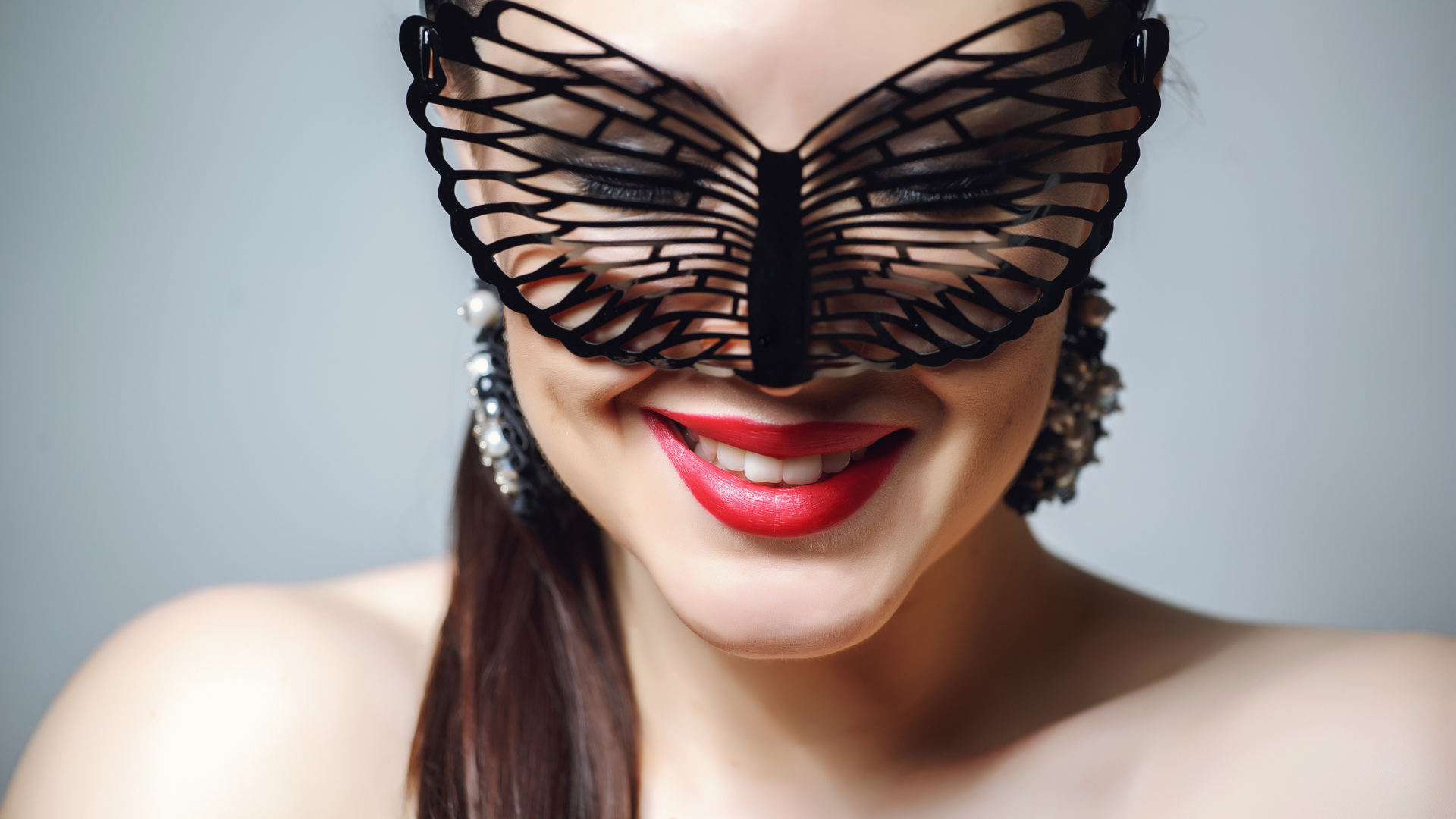 Улыбающаяся девушка в черной маске на сером фоне