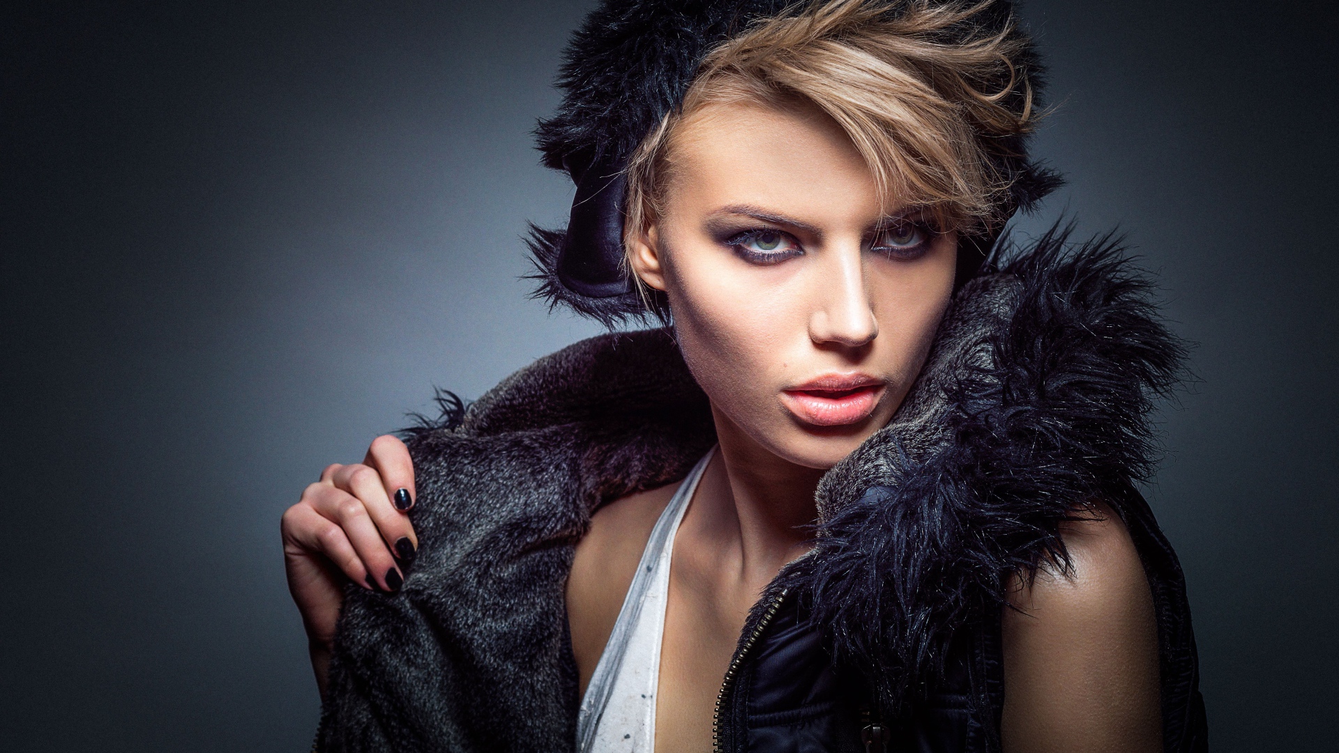 Девушка в теплой жилетке и шапке на сером фоне