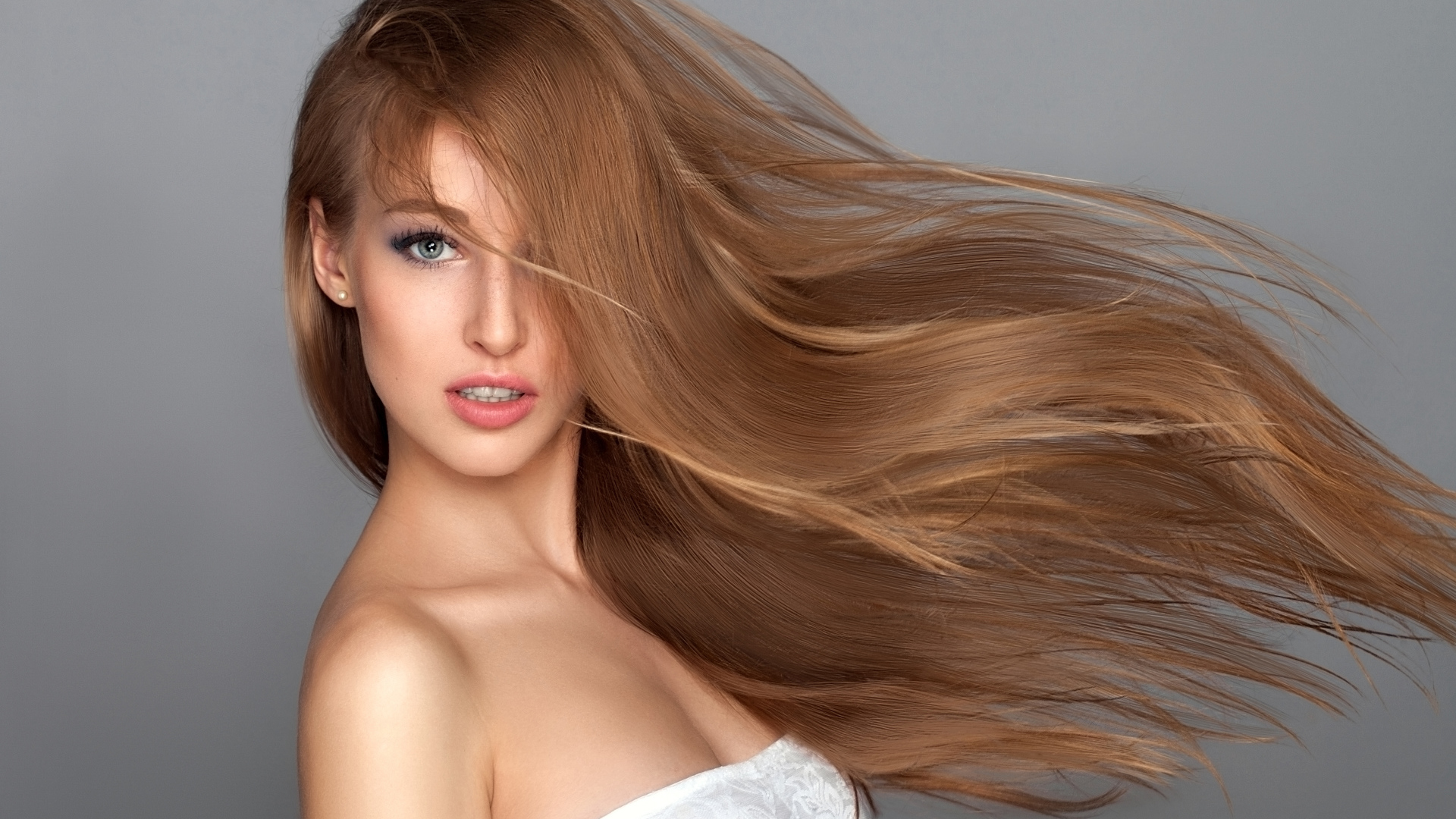 Ветер развивает волосы красивой девушки на сером фоне