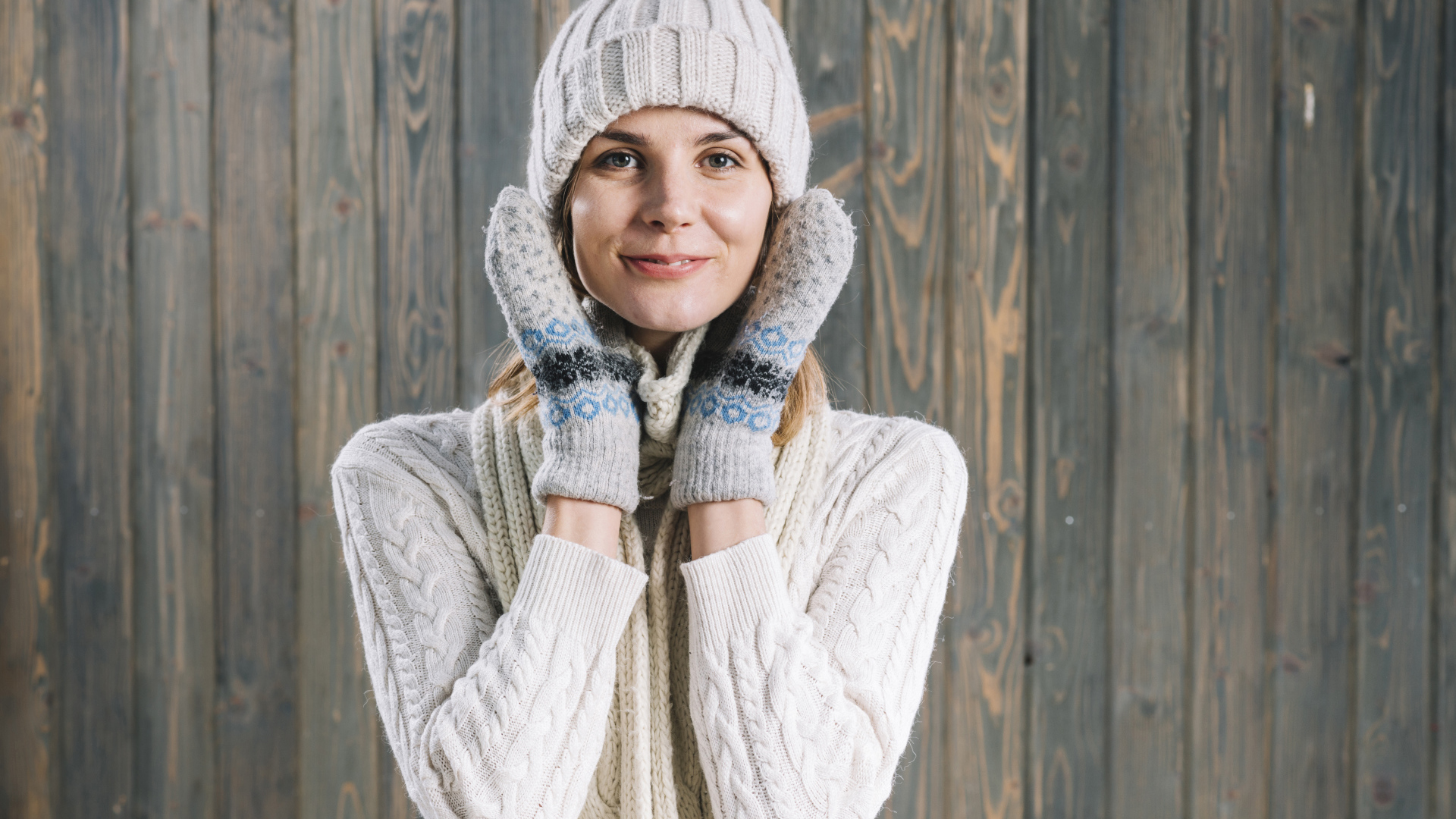 Молодая девушка на шапке, варежках  и теплой шапке на фоне забора