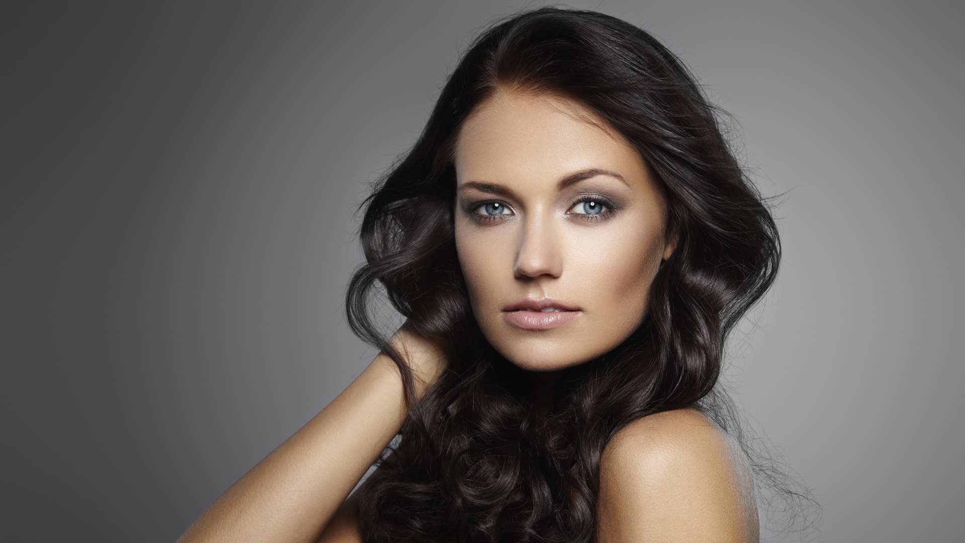 Молодая настоящая голубоглазая длинноволосая брюнетка на сером фоне