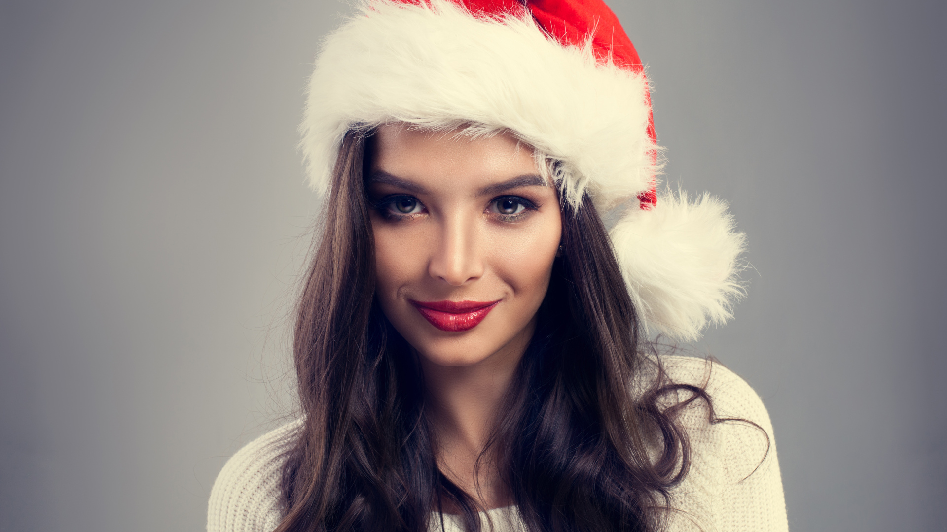 Красивая брюнетка в новогодней шапке на сером фоне