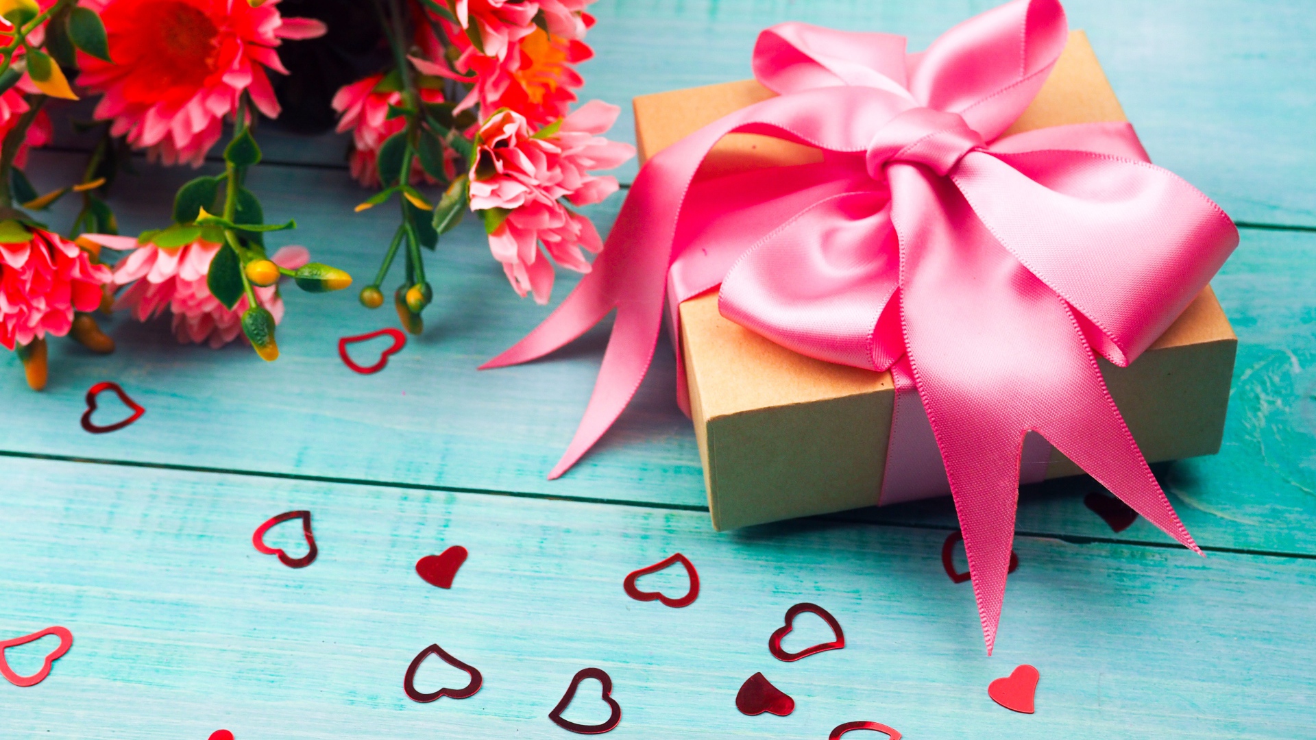 Gift with a pink bow on a blue table with a bouquet