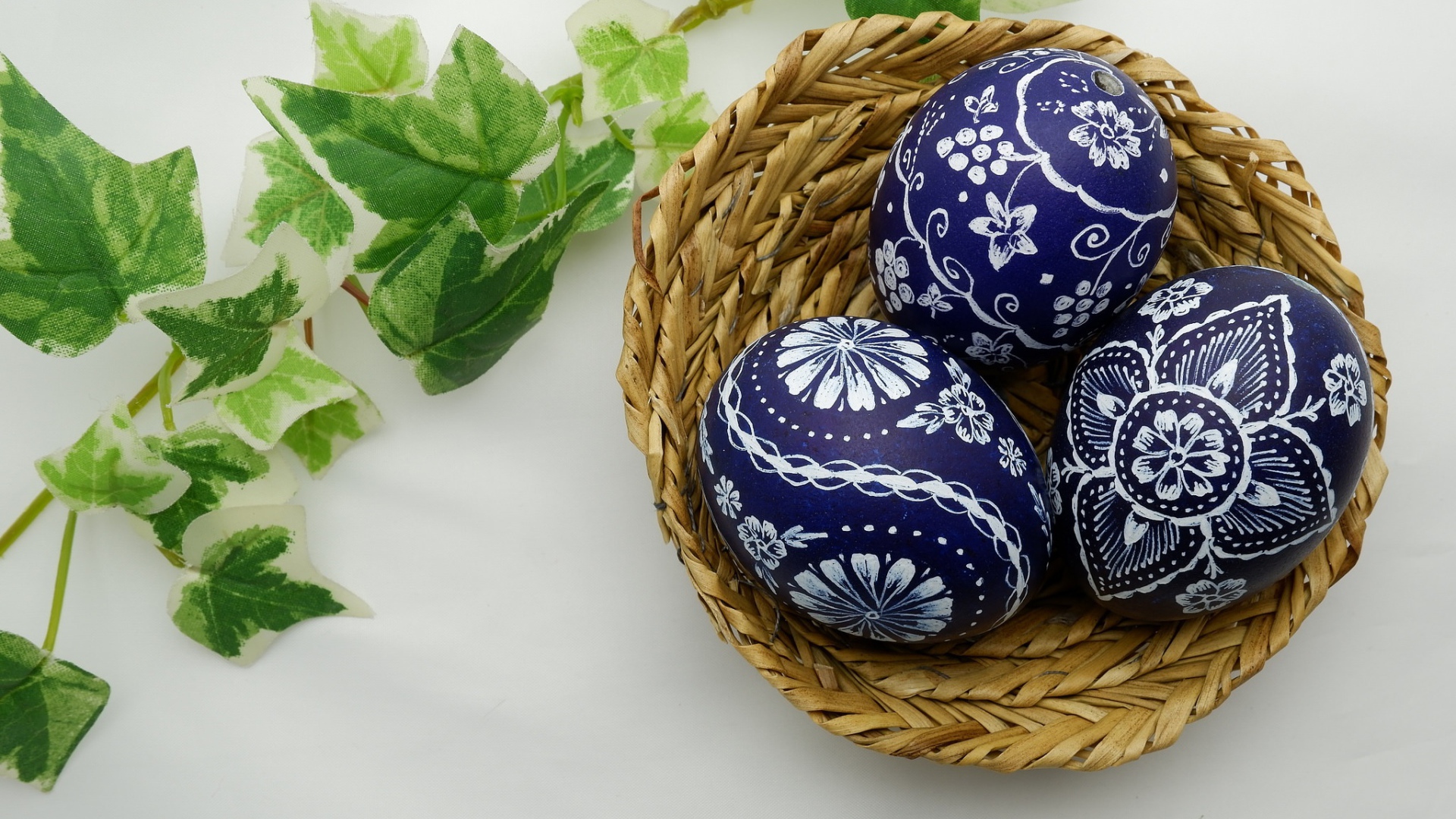 Три раскрашенных яйца в корзинке на столе с веткой 