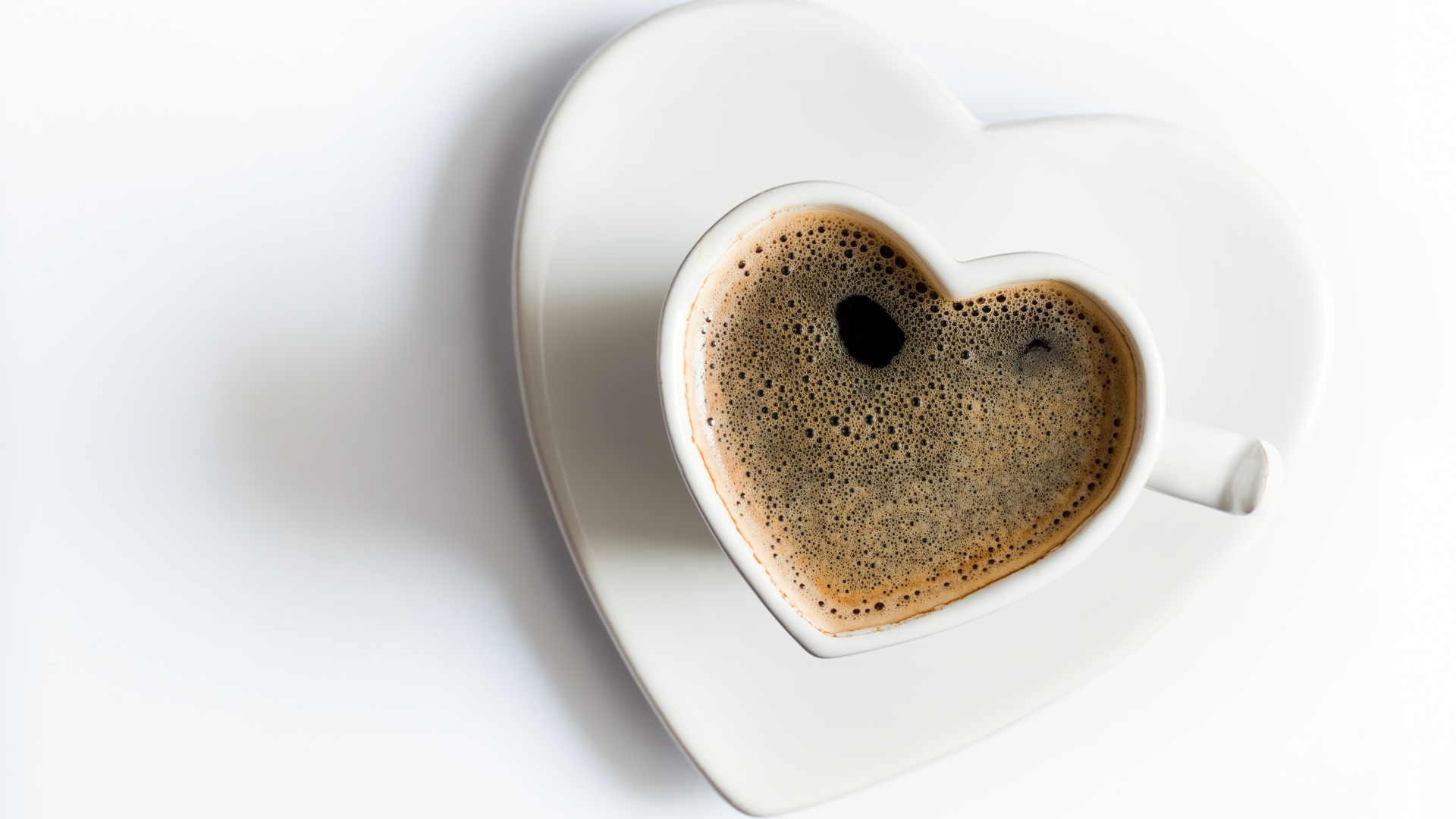 Красивая белая чашка в форме сердца с кофе на белом фоне
