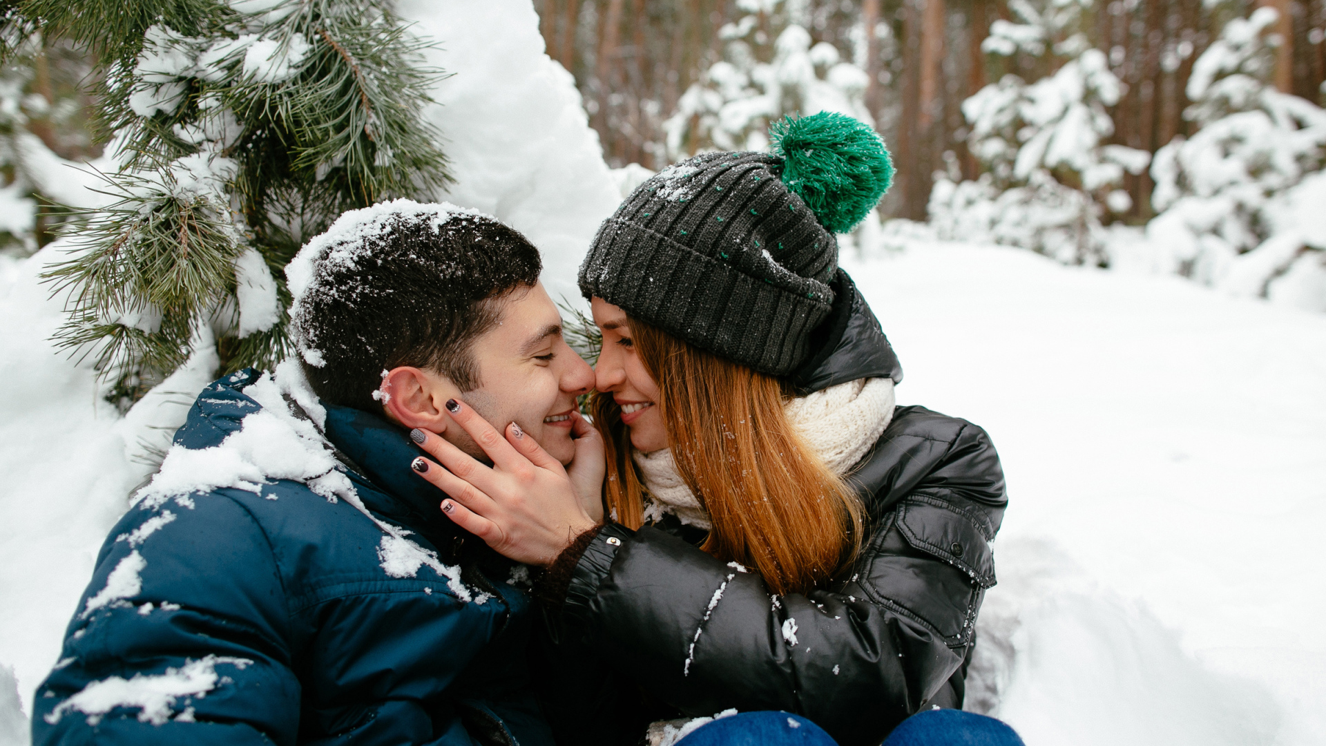 Влюбленная пара сидит под заснеженной еловой веткой зимой