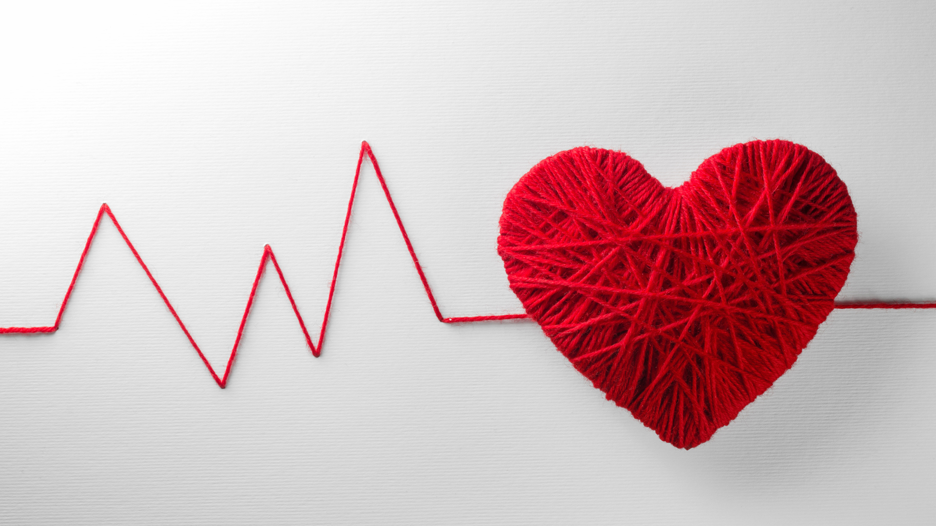 Красное сердце из нитей на сером фоне 