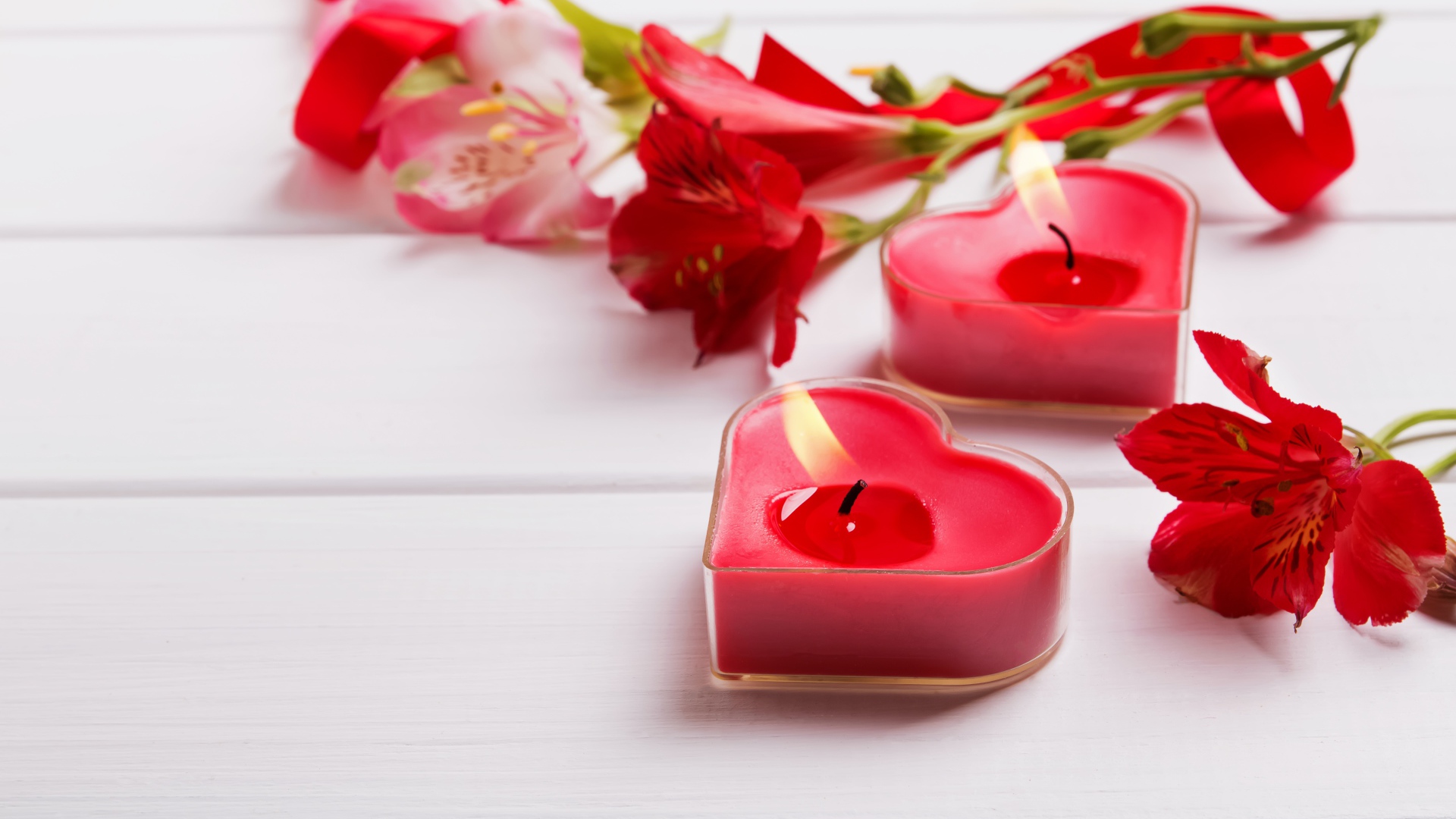 Две красные свечи в форме сердца на столе с цветами альстромерии 