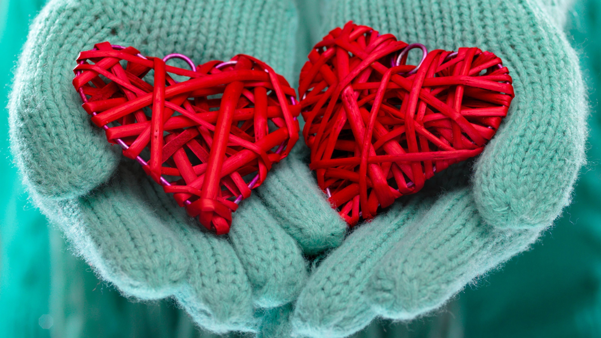 Два плетеных красных сердца лежать на руках в варежках