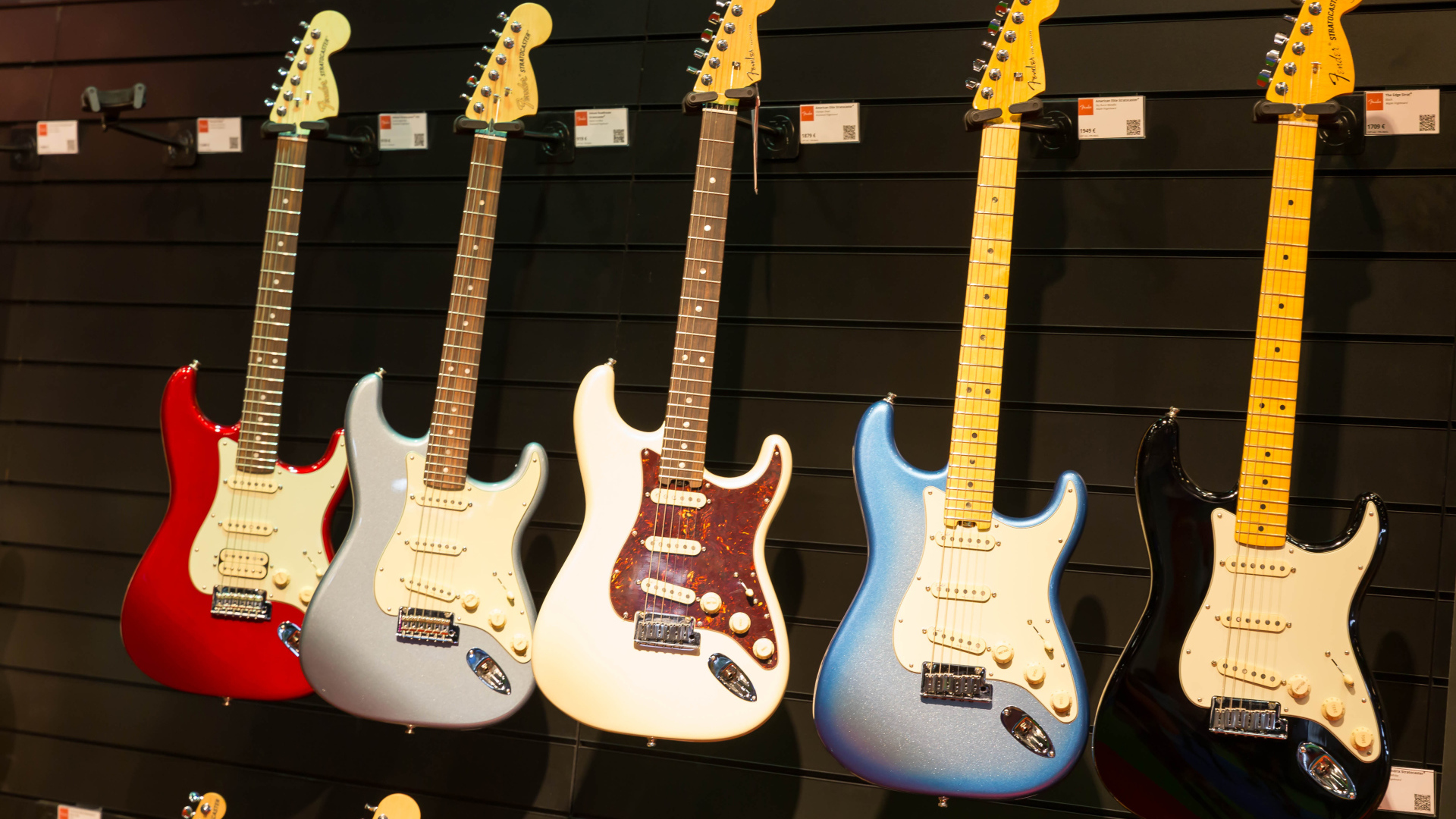 Много разноцветных электрогитар на стене 