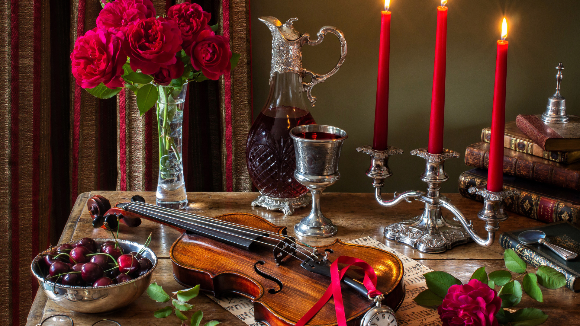 Зажженные красные свечи на столе букетом роз, скрипкой и черешней 