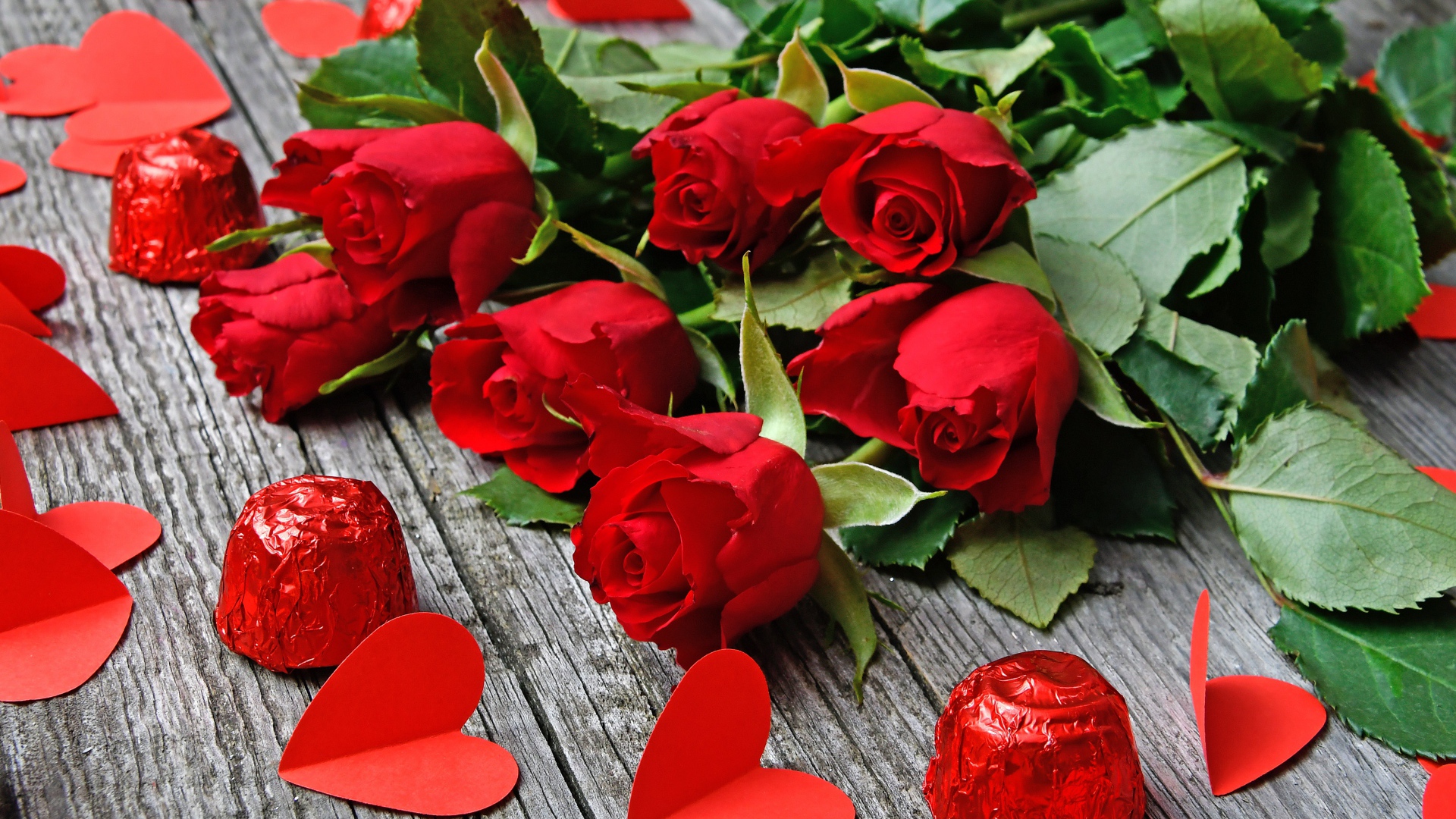 Букет красных роз на деревянном столе с конфетами и красными сердечками