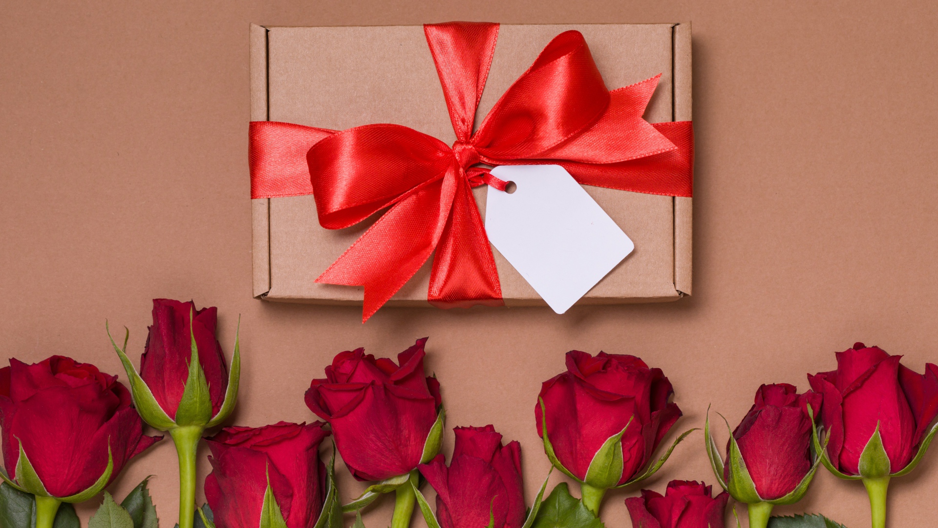 Подарок с красным бантом на бежевом фоне с красными розами