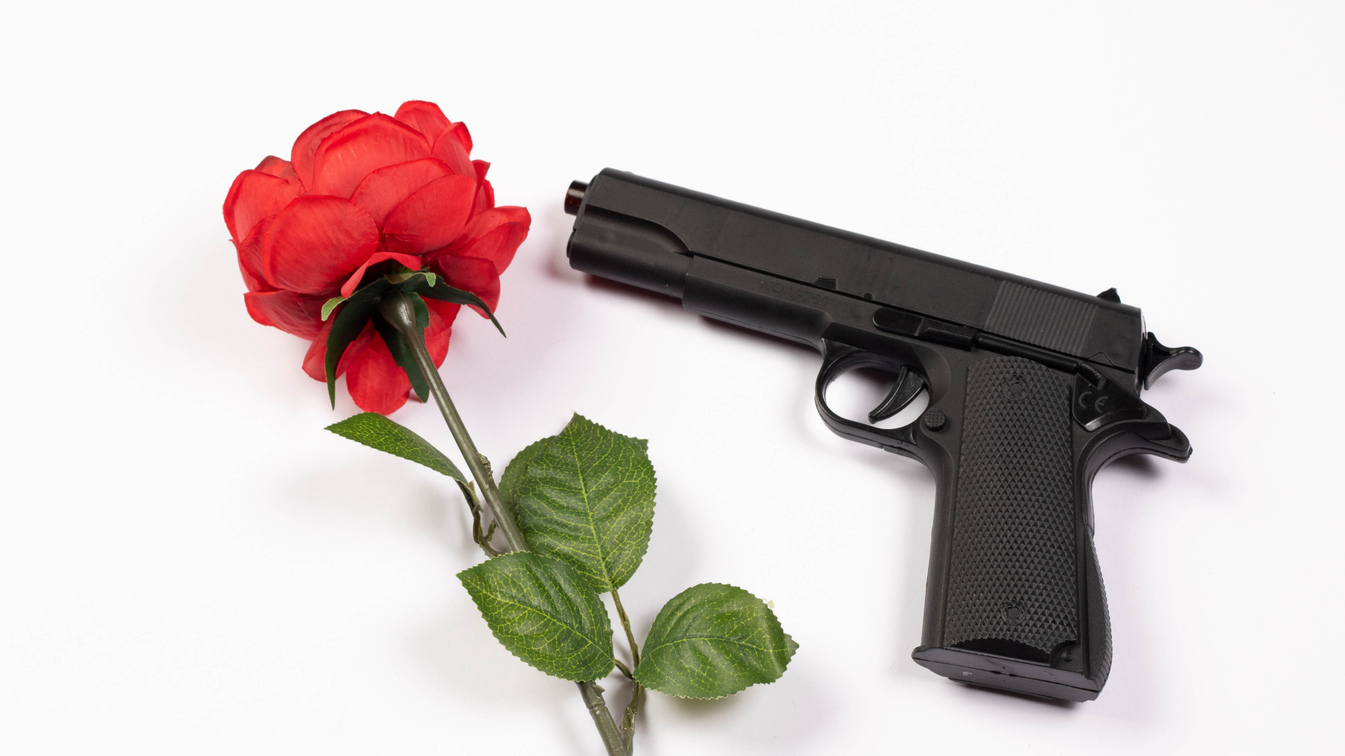 Красная роза и черный пистолет на белом фоне