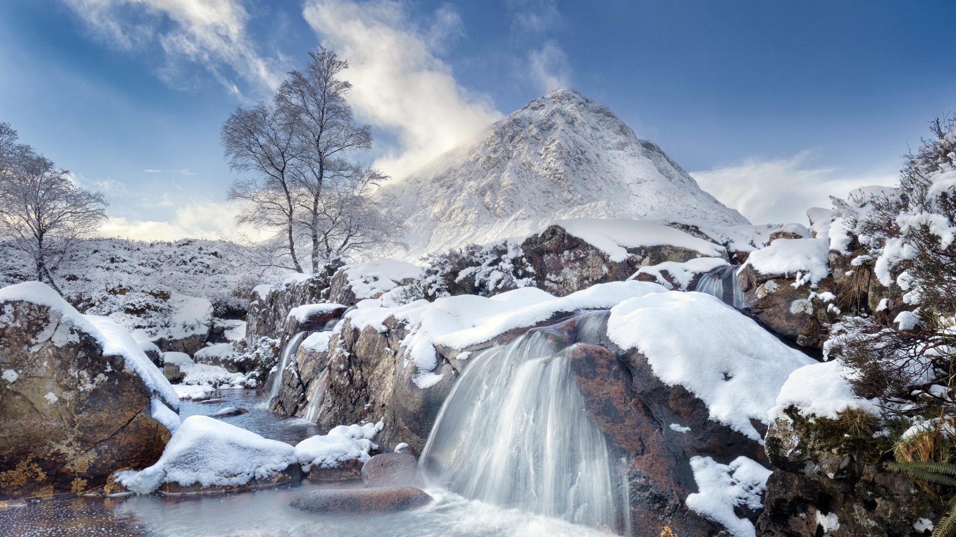 Водопад стекает с камней на фоне заснеженной горы