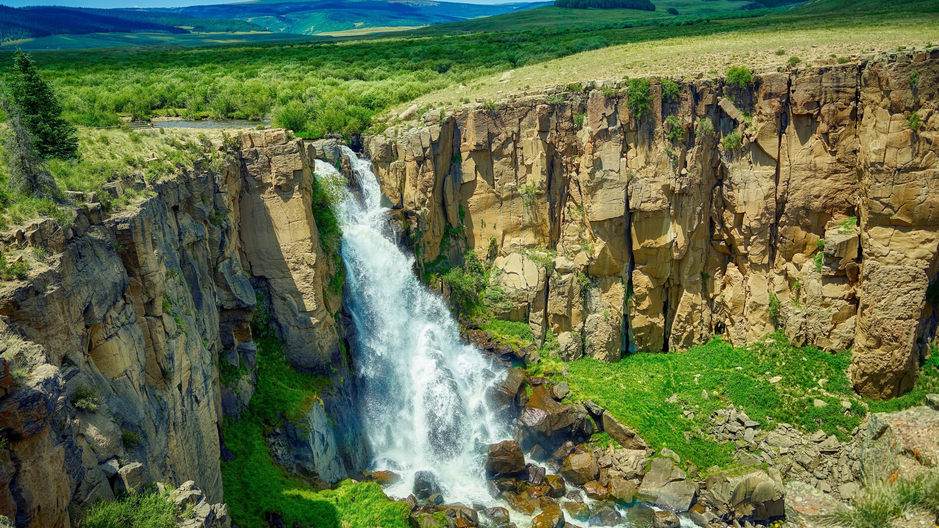 Быстрая вода водопада стекает по утесу на фоне голубого неба