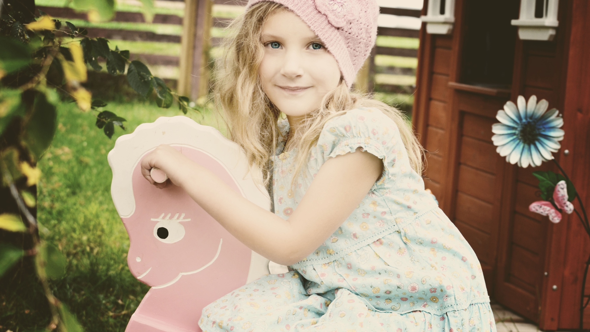 Девочка в платье сидит на деревянной лошади