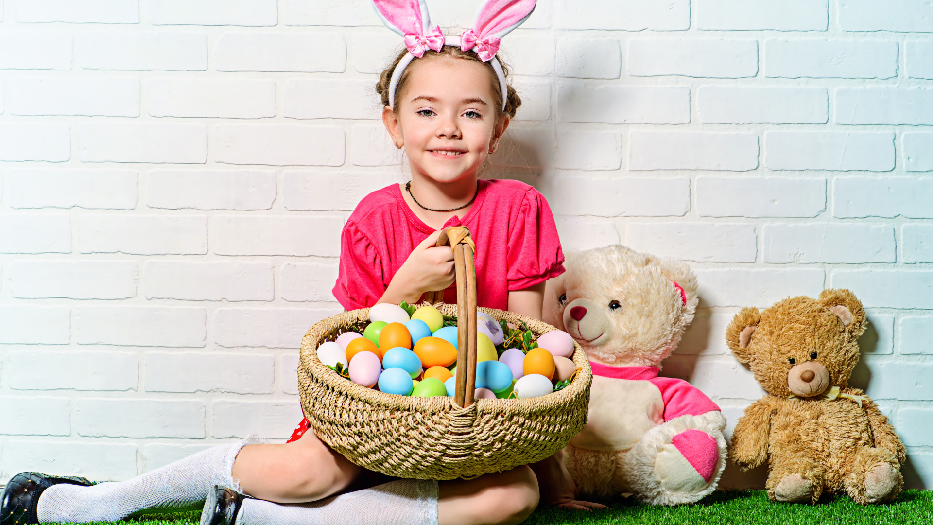Улыбающаяся девочка сидит у стены с корзиной пасхальных яиц и игрушками