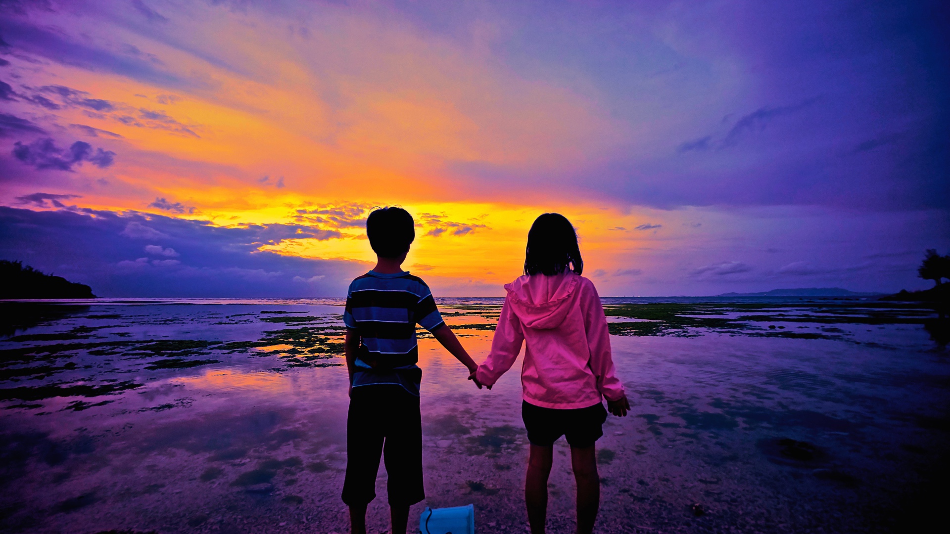 Маленькие мальчик и девочка стоят у воды на фоне заката 