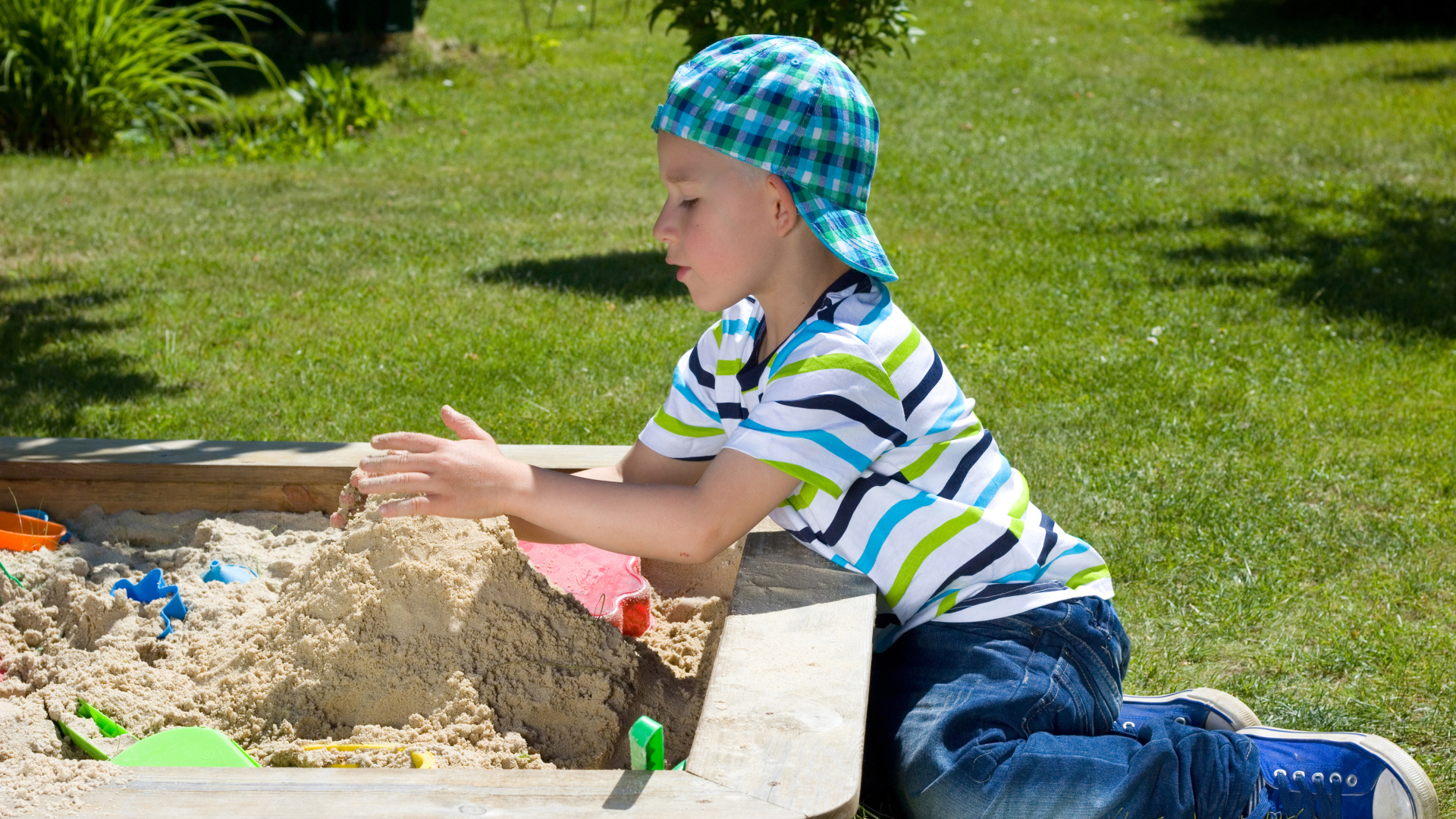 Маленький мальчик играет в песке на зеленой траве