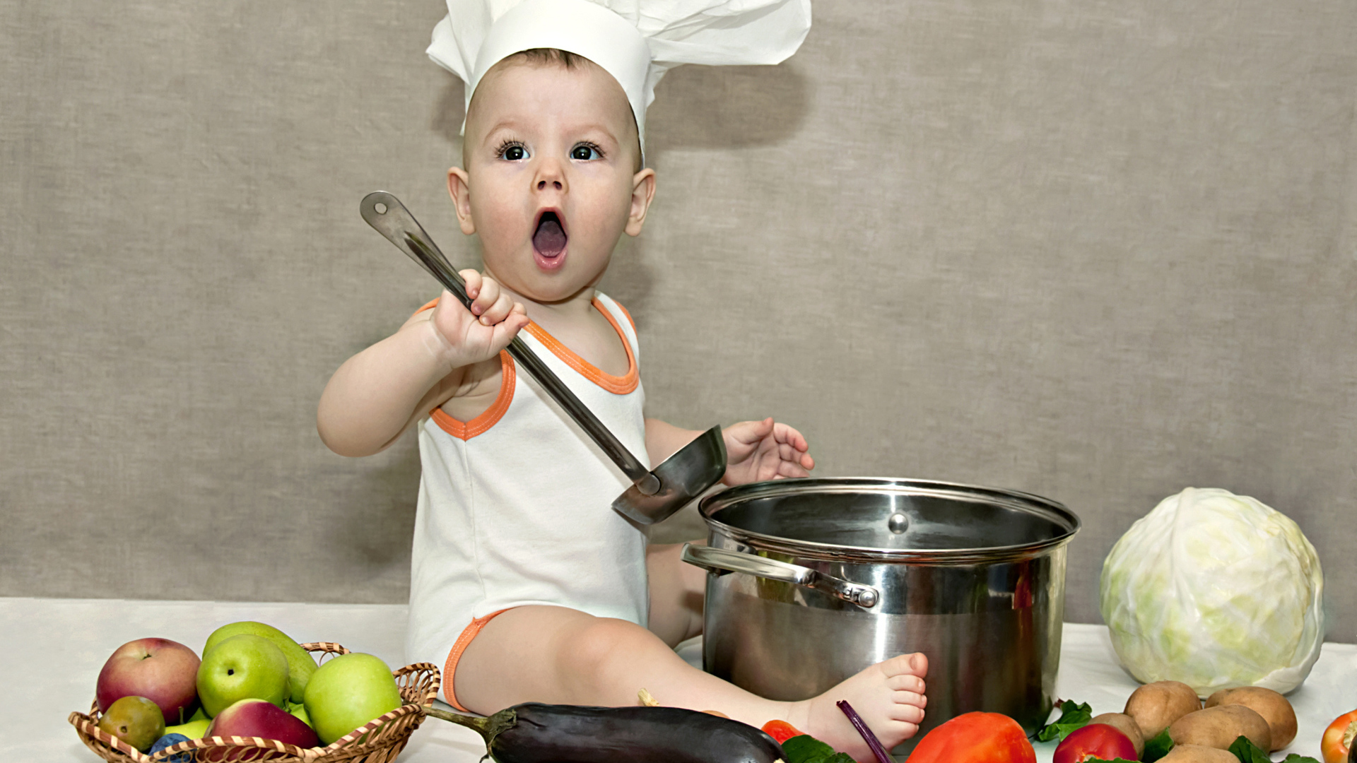 Маленький поваренок с кастрюлей на столе с овощами