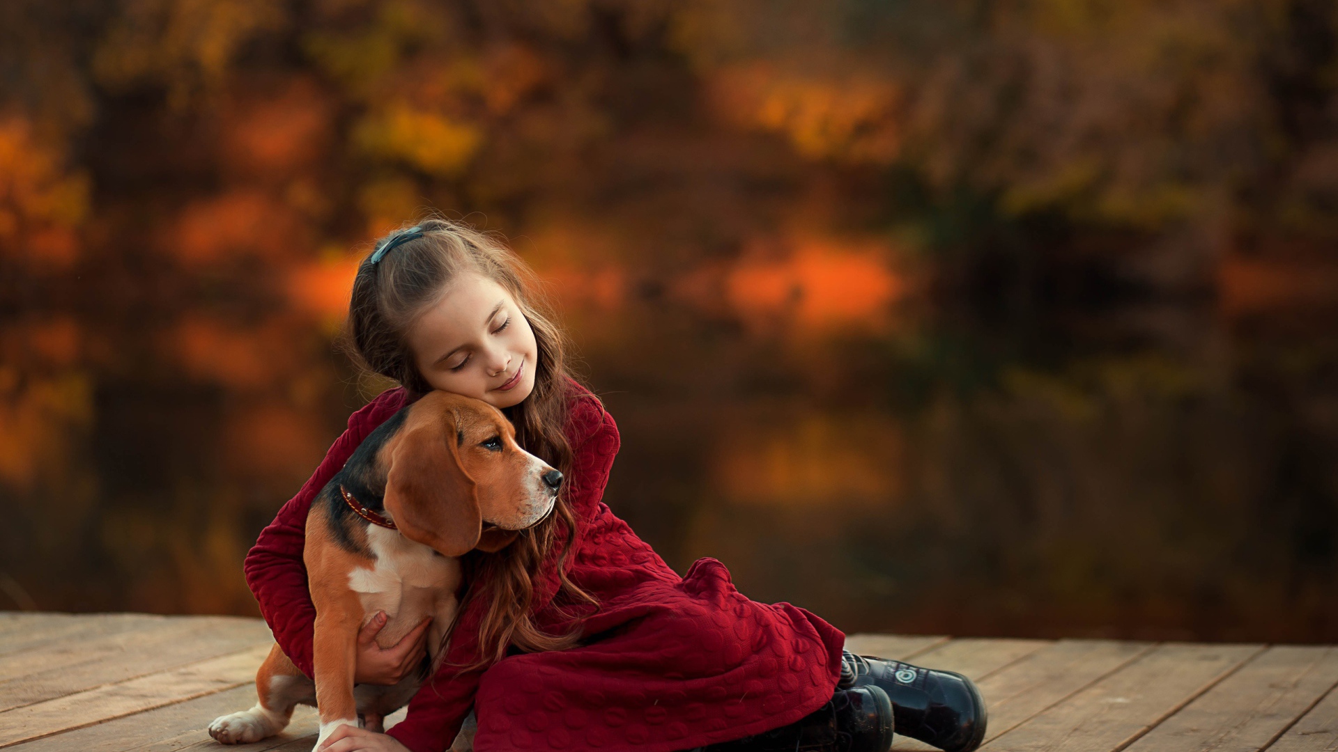 Маленькая девочка обнимает собаку породы бигль на мосту