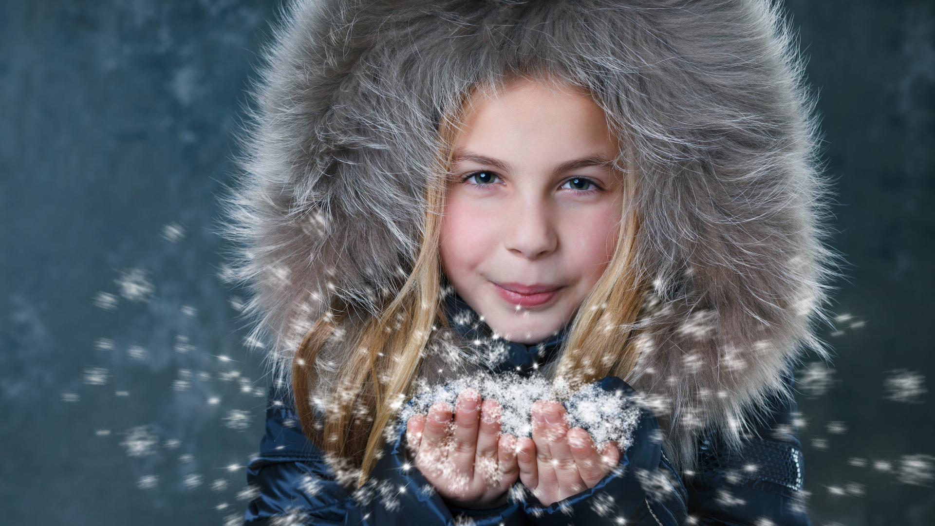 Маленькая девочка в капюшоне сдувает снежинки с ладоней