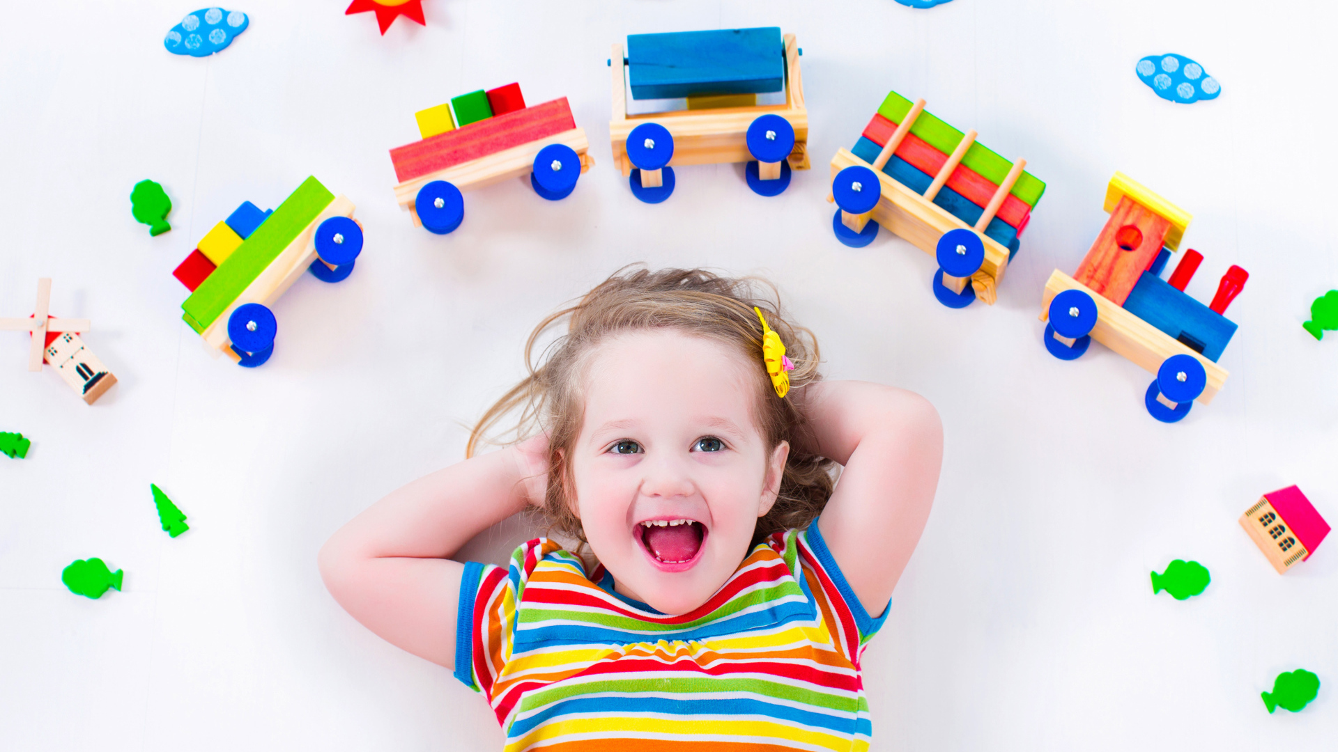 Маленькая девочка на сером фоне с игрушечным паровозом 