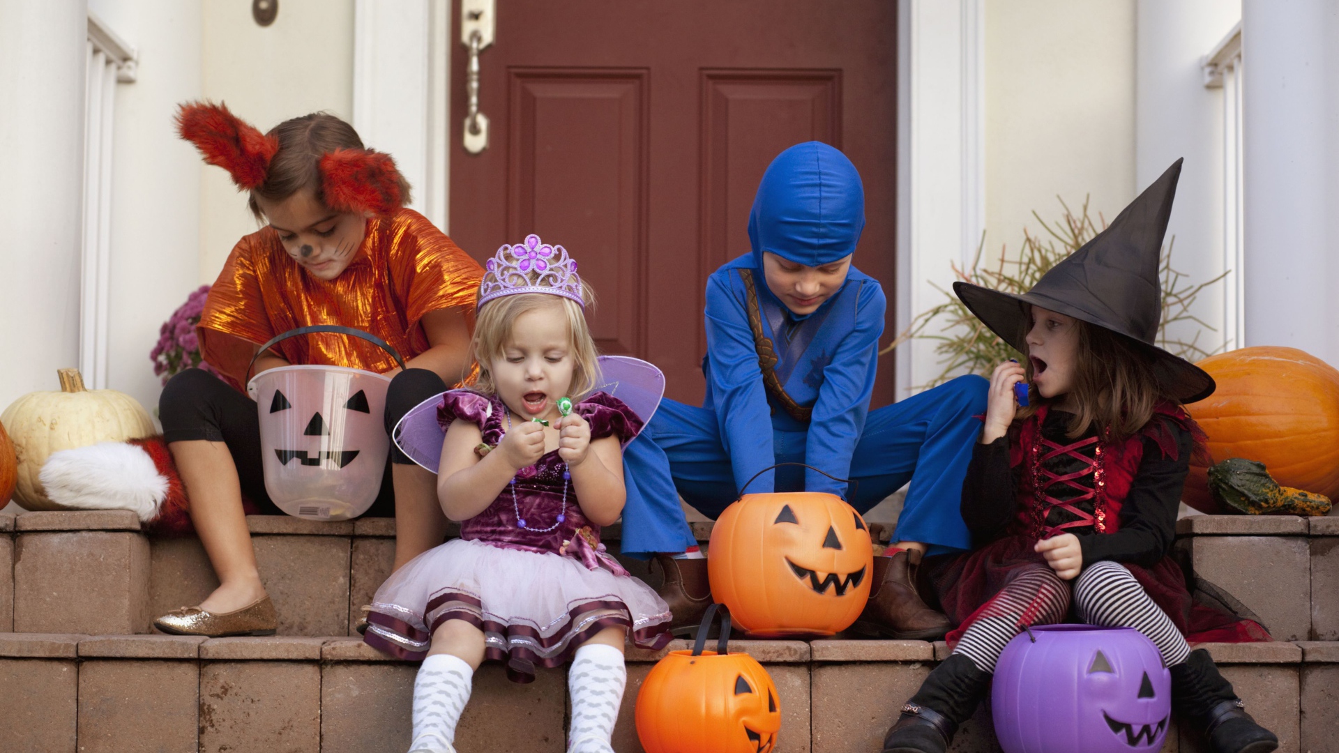 Маленькие дети в костюмах на Хэллоуин сидят на ступеньках со сладостями