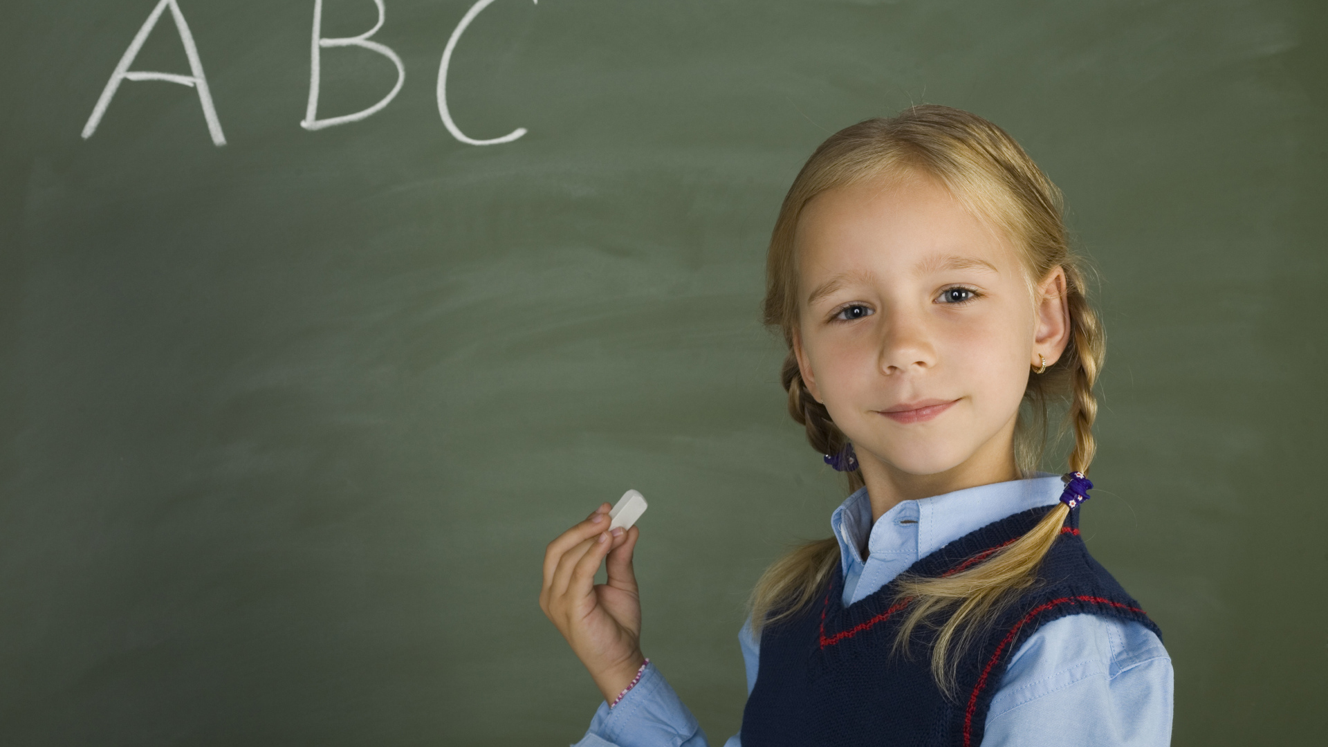 Маленькая школьница пишет буквы на доске 