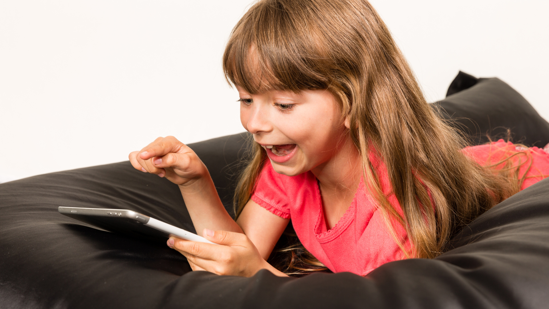 Маленькая улыбающаяся девочка лежит с планшетом