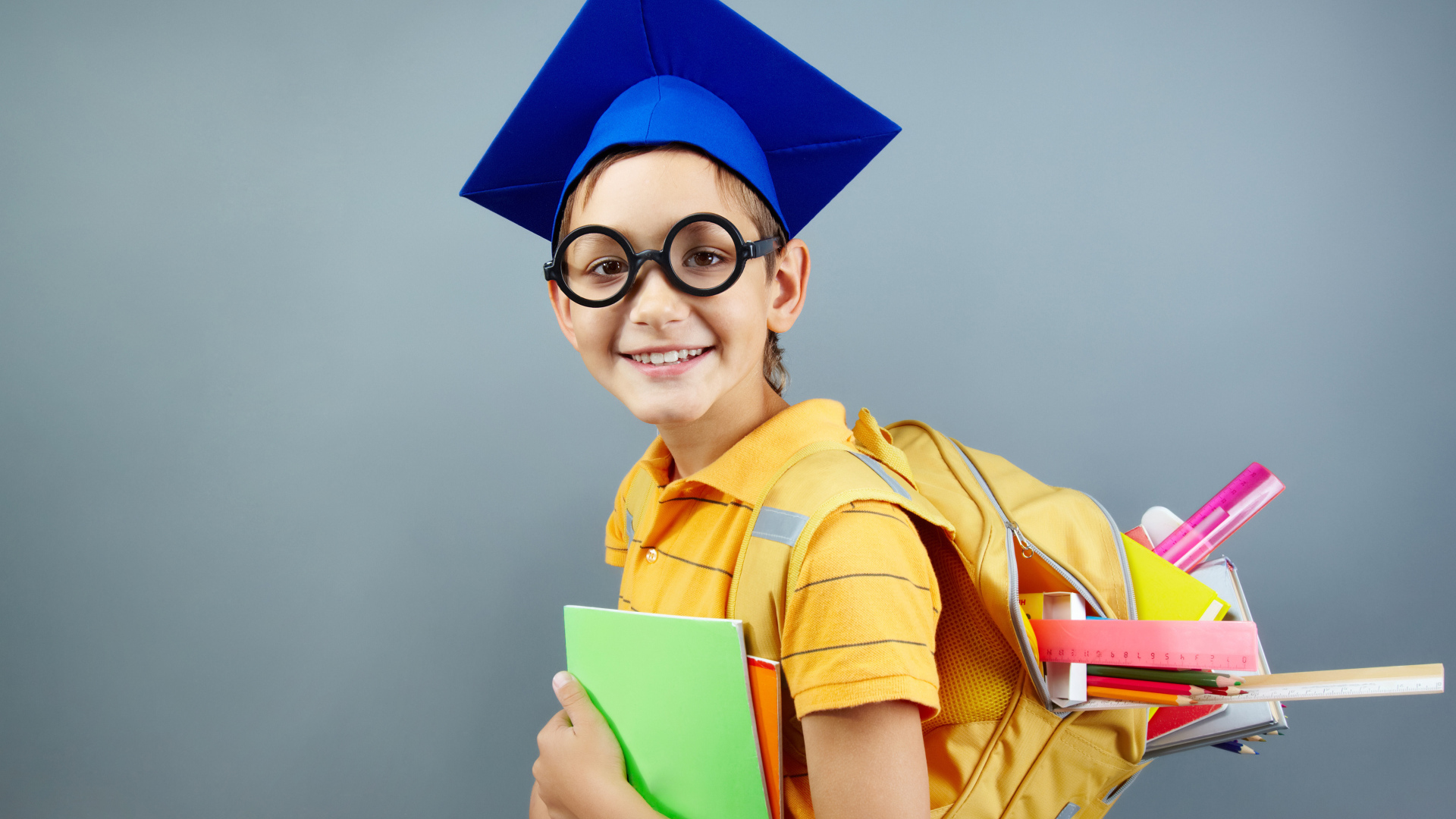 Умный школьник в очках со школьными принадлежностями на сером фоне