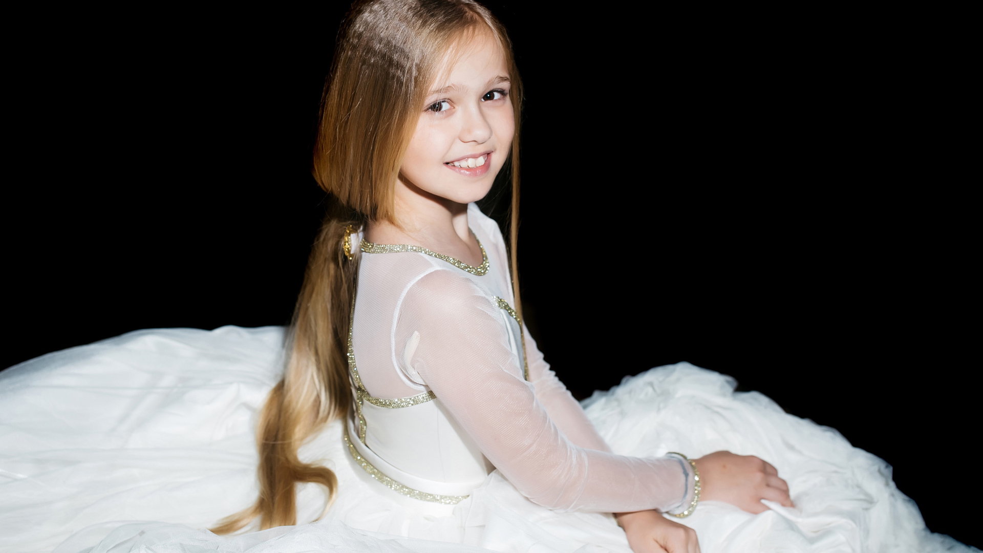 Улыбающаяся девочка в красивом белом платье на черном фоне