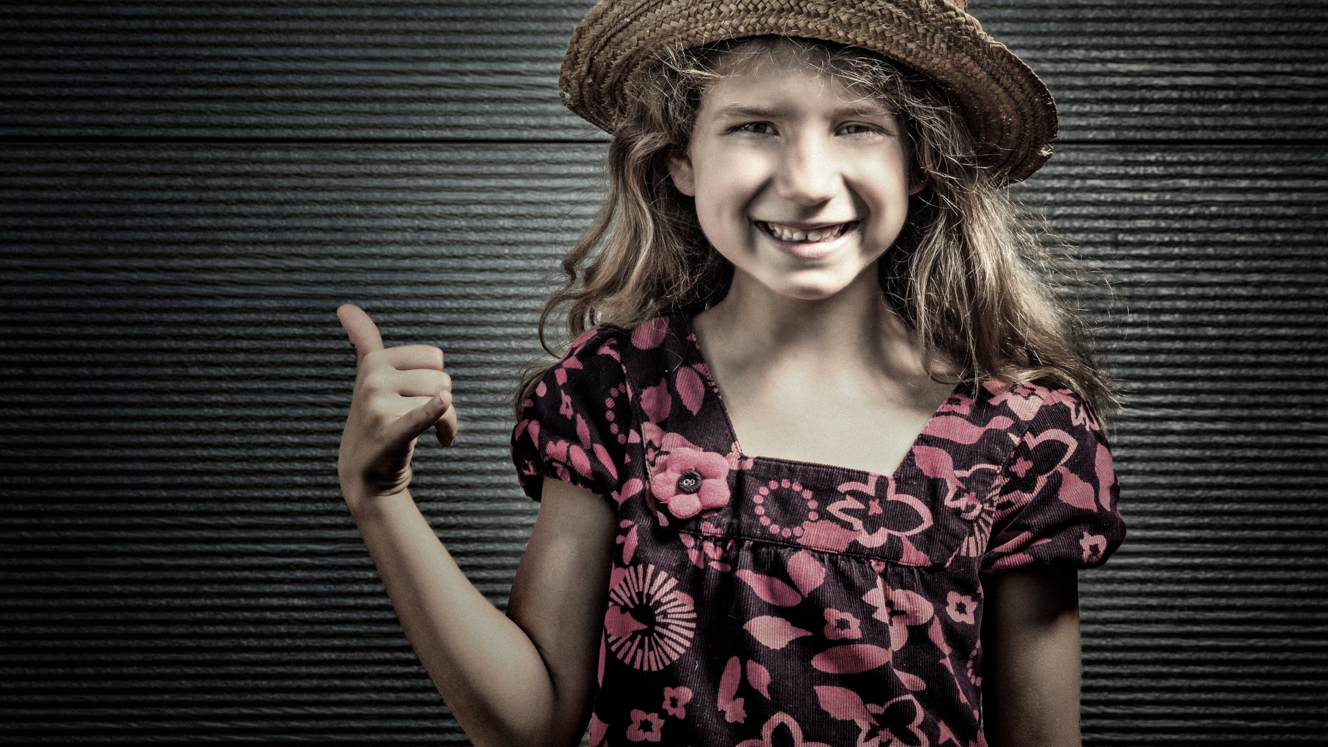 Улыбающаяся девочка в соломенной шляпе у стены 