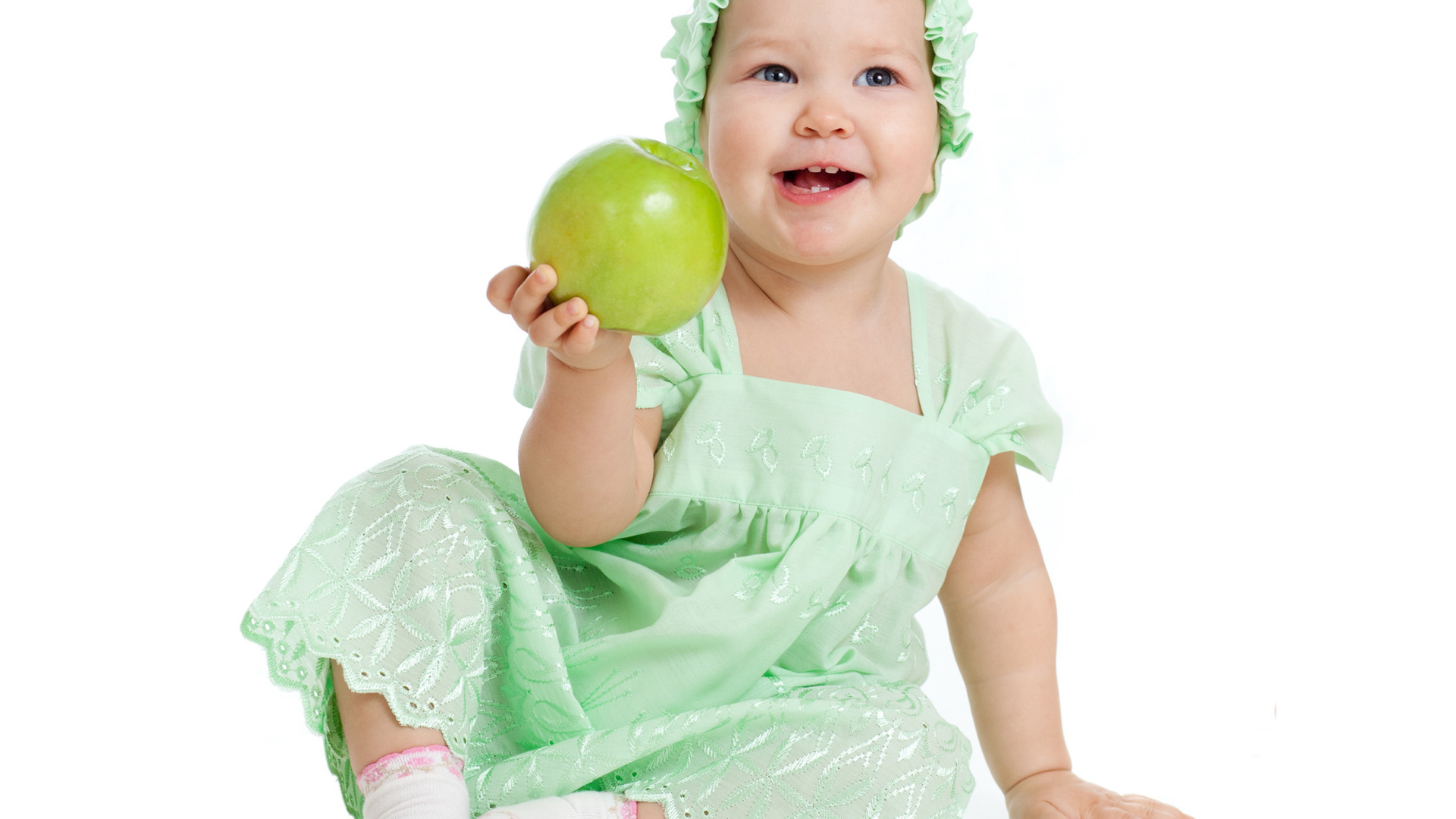 Улыбающаяся маленькая девочка в красивом платье с зеленым яблоком в руке