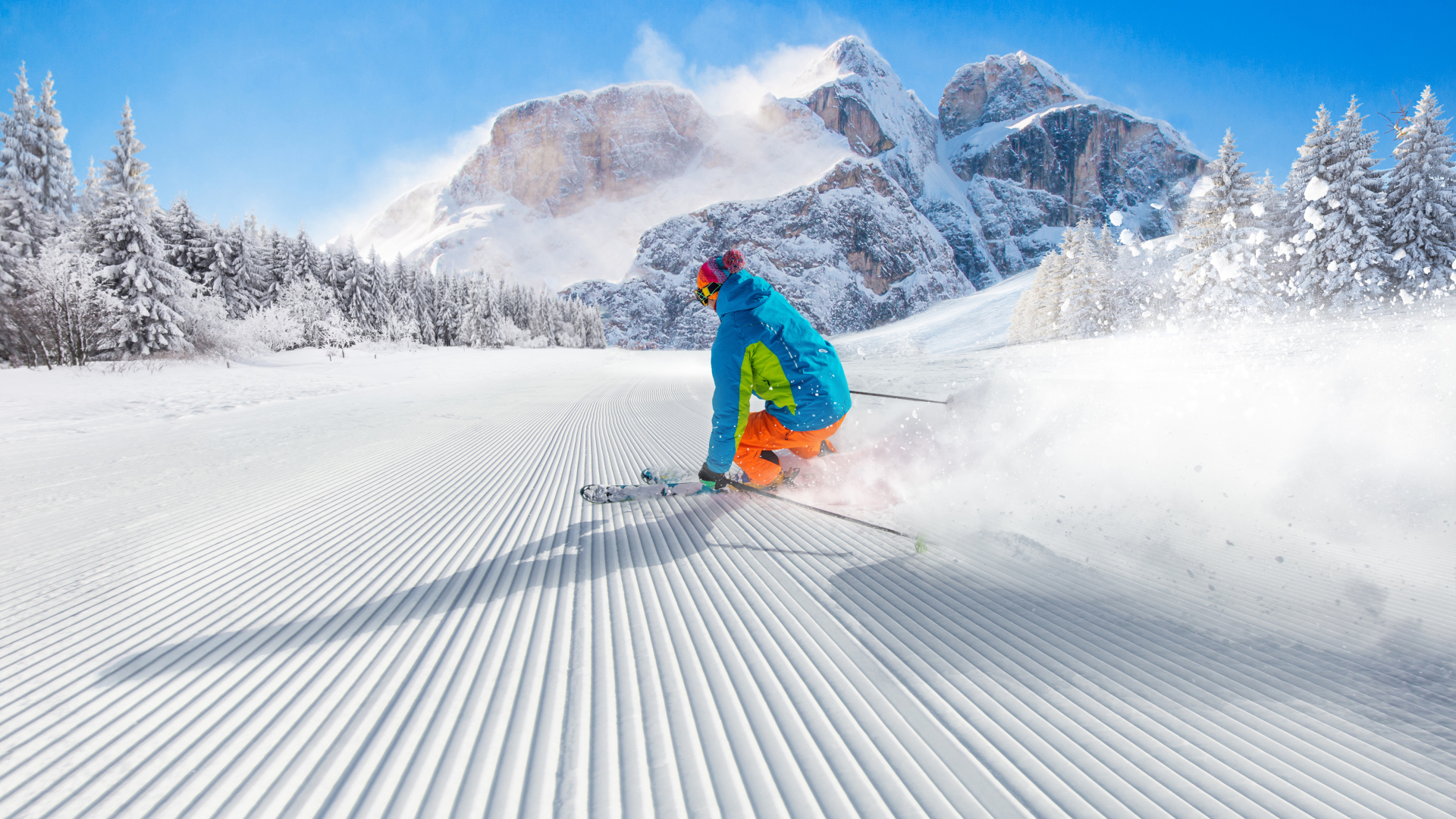 Лыжник спускается по склону на фоне заснеженных гор 