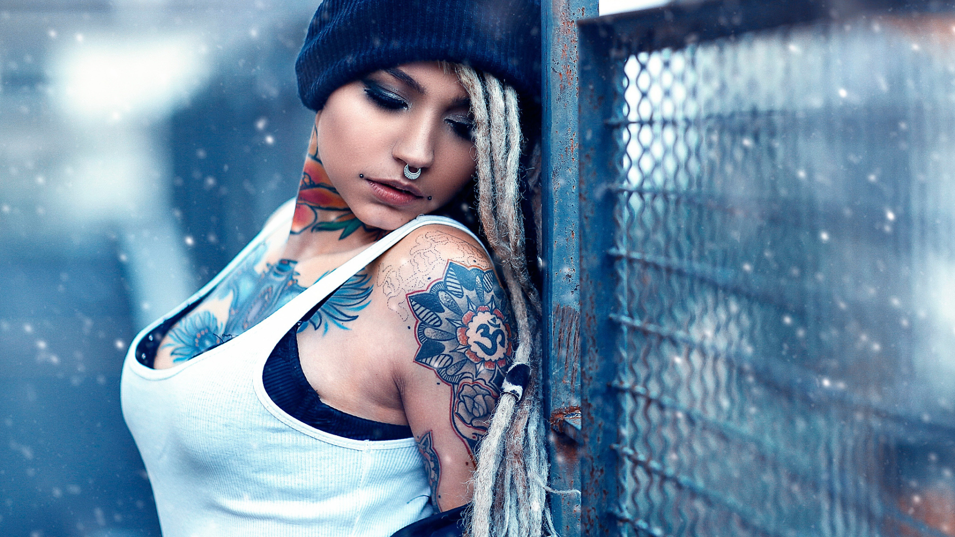 Девушка с татуировками на шее и пирсингом в носу у забора