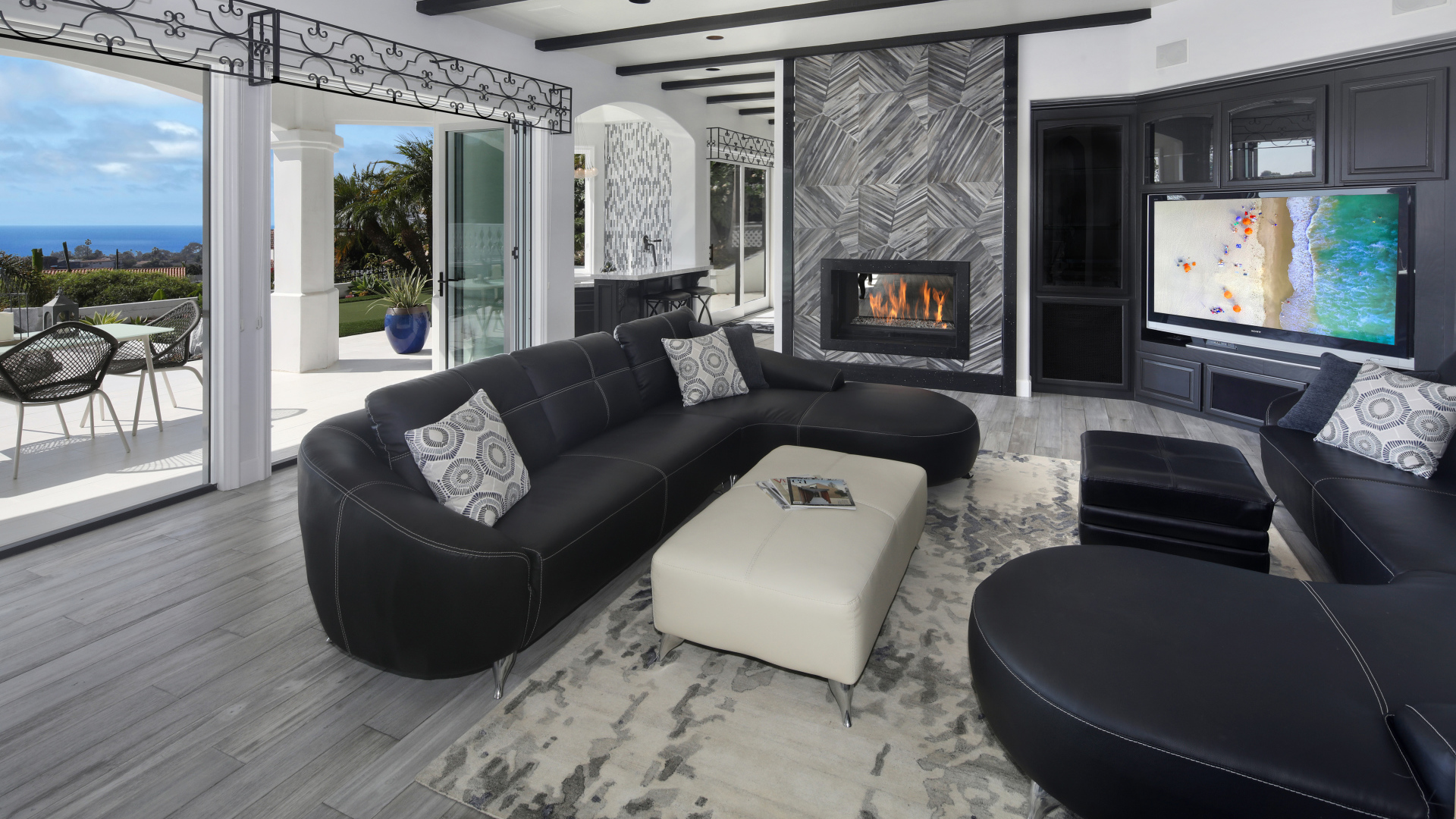 Большая просторная гостиная с черными кожаными диванами, телевизором и камином 