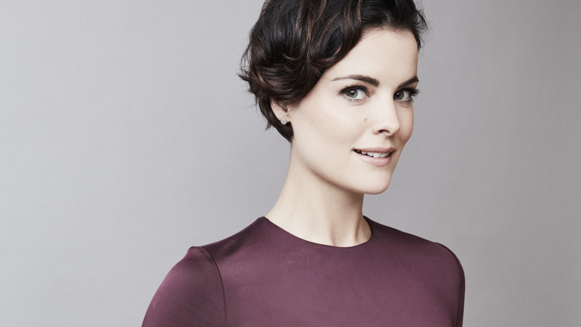 Улыбающаяся девушка, актриса Джейми Александр на сером фоне